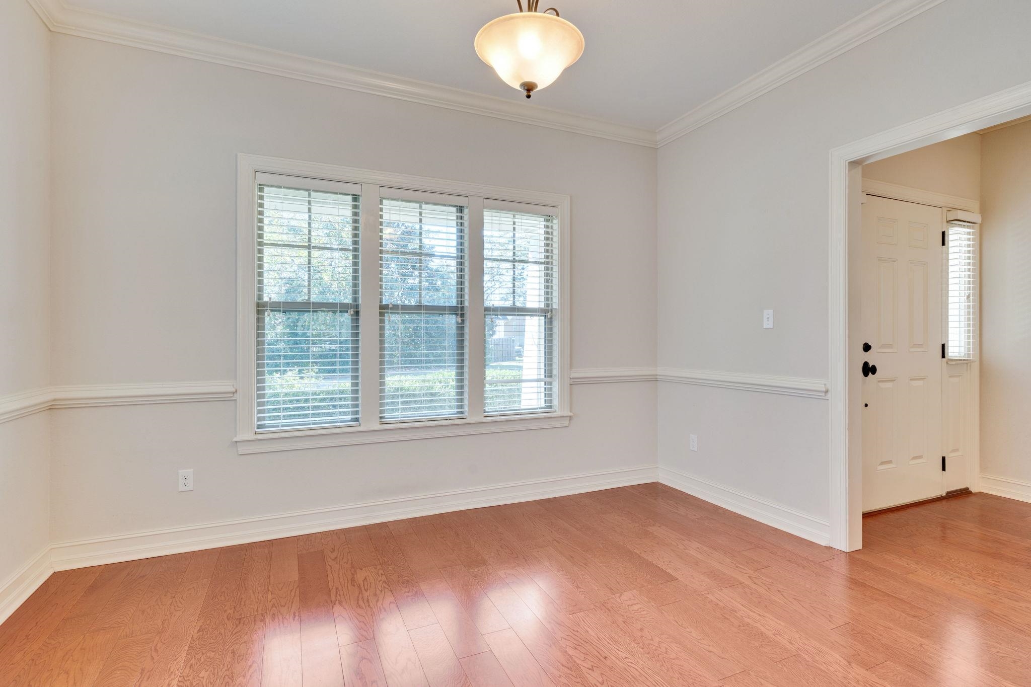 Empty entry room with hardwood floors, three shaded windows, and a paneled front door.