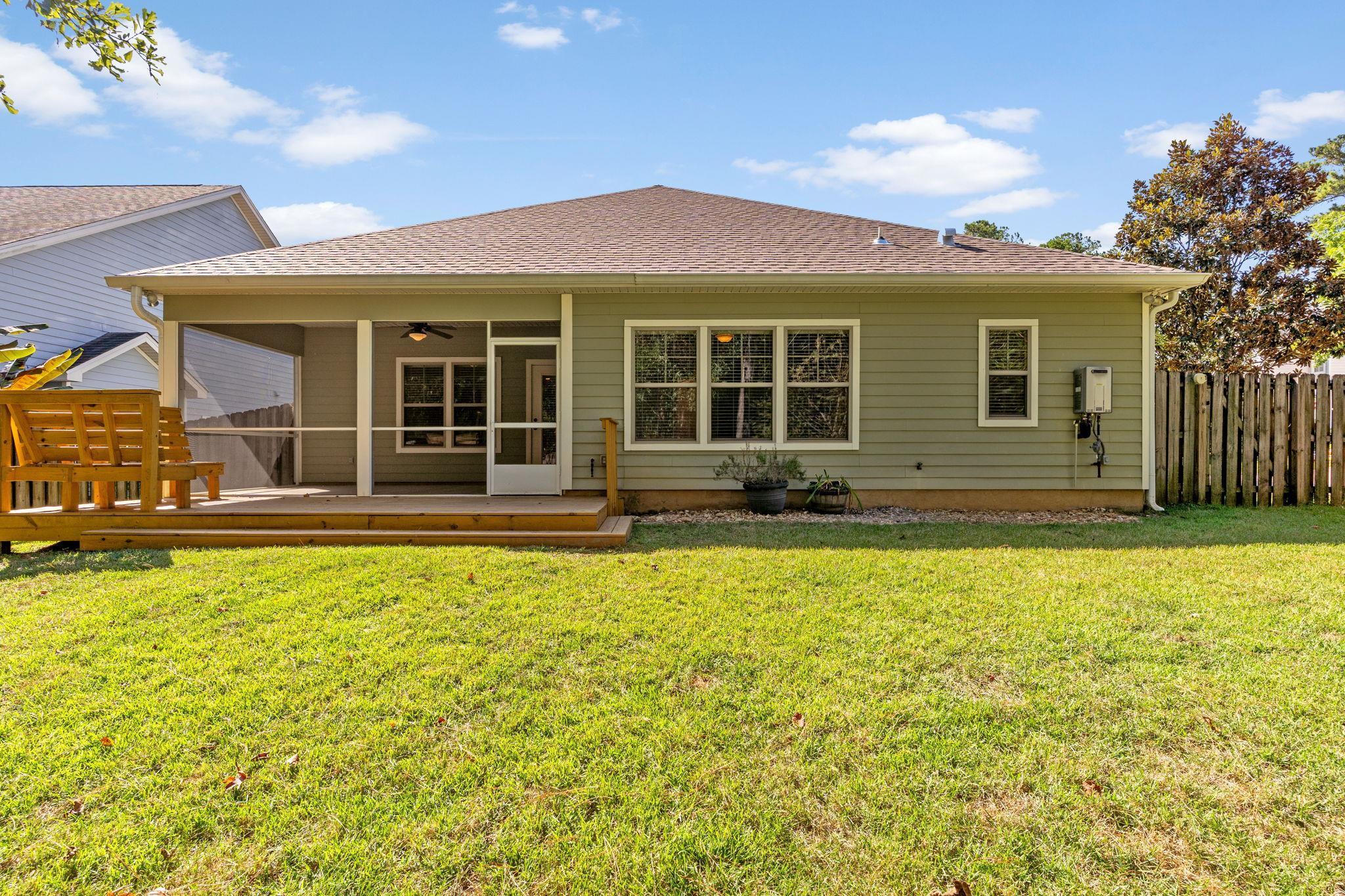 Rear of an olive-green house with a covered screened porch, wooden deck, and broad lawn.