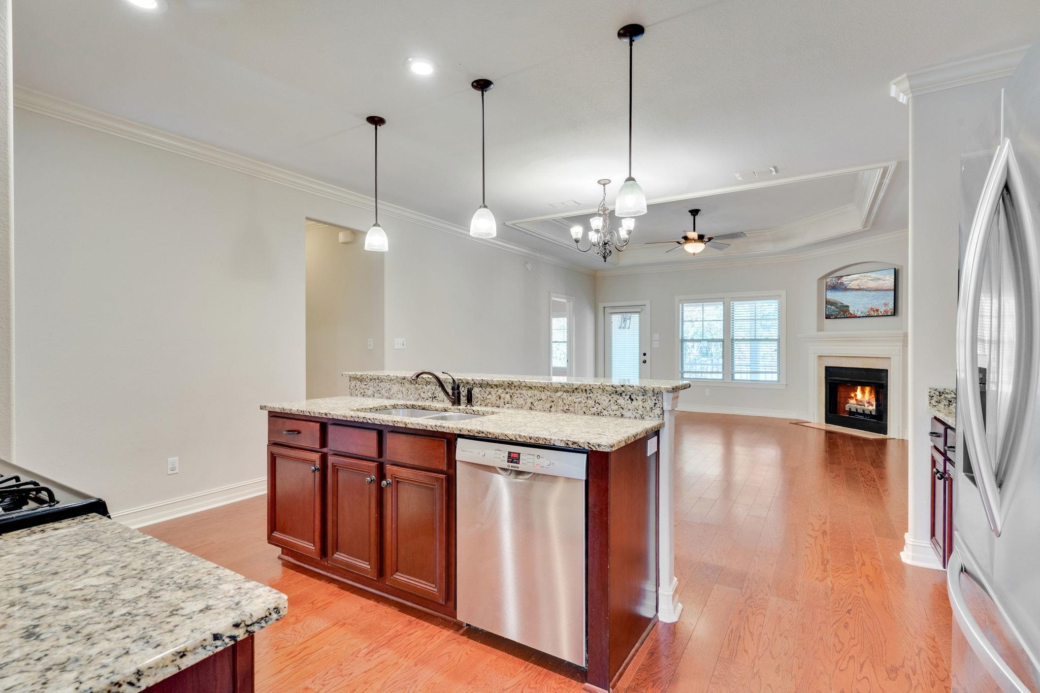 Open kitchen with granite counters and wood cabinets, leading to a living area with a lit fireplace.