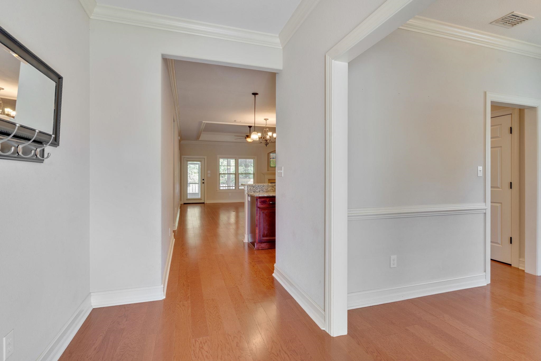 Entry hall with hardwood floors leading to a kitchen island and chandelier-lit dining area.