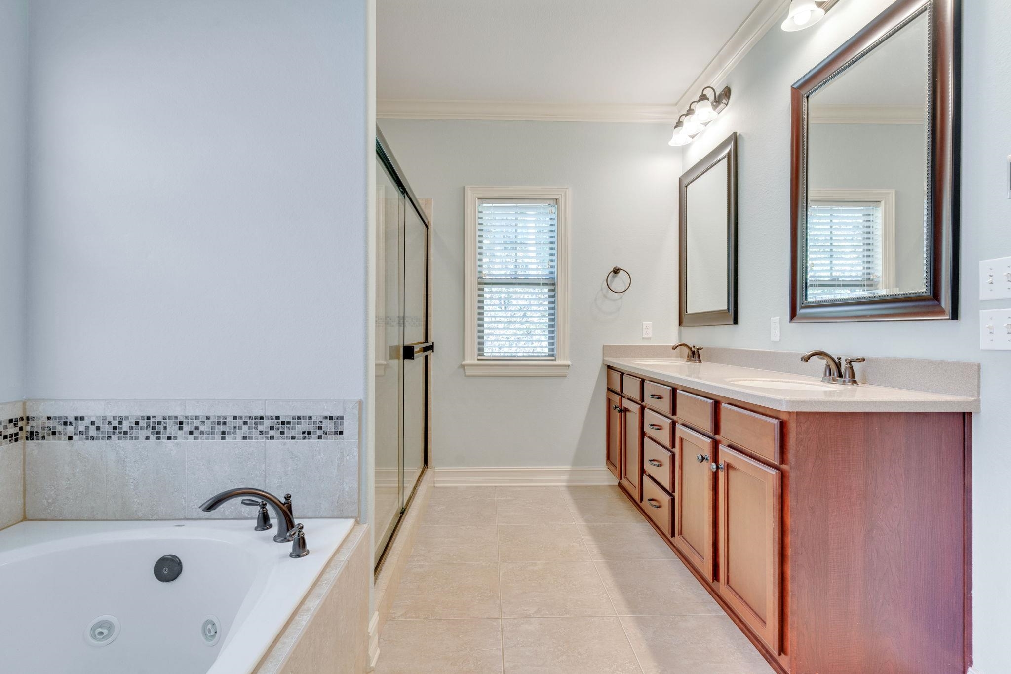 Bathroom with a wood double vanity, jetted bathtub, and glass-enclosed shower.