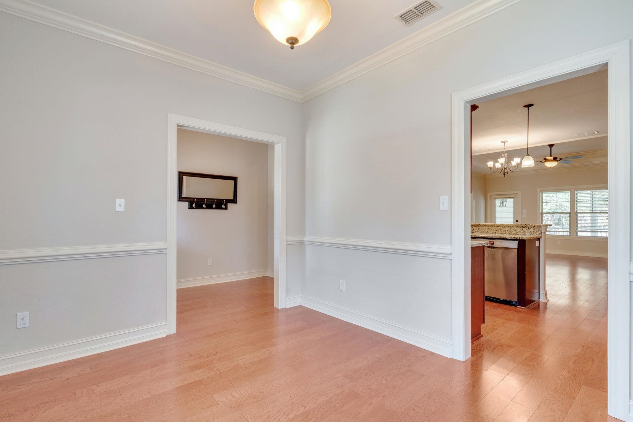 Empty dining room with hardwood floors and trim, opening to a kitchen with a granite island.