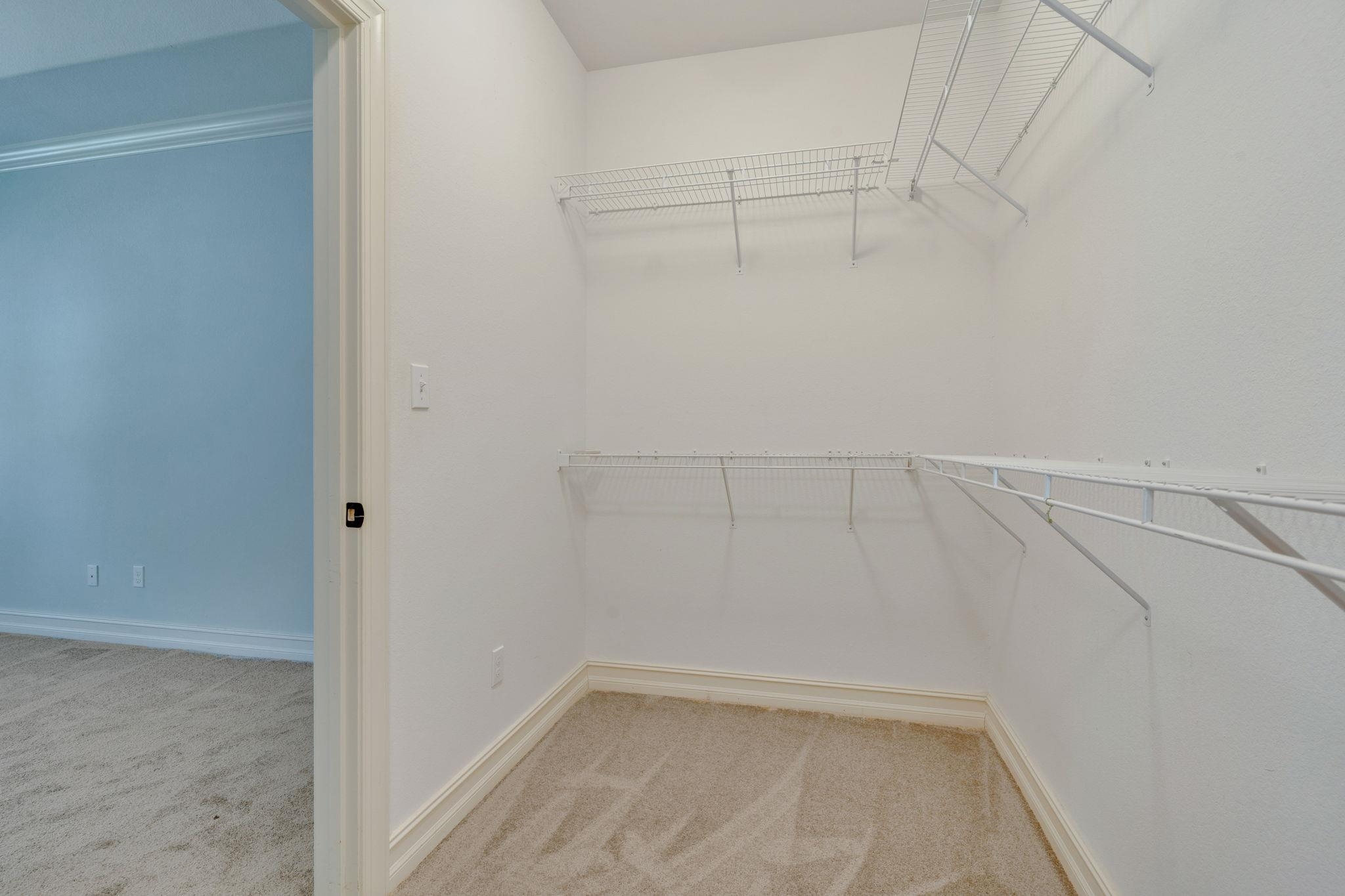 Empty walk-in closet with wire shelving and beige carpet, viewed from the doorway to a blue room.