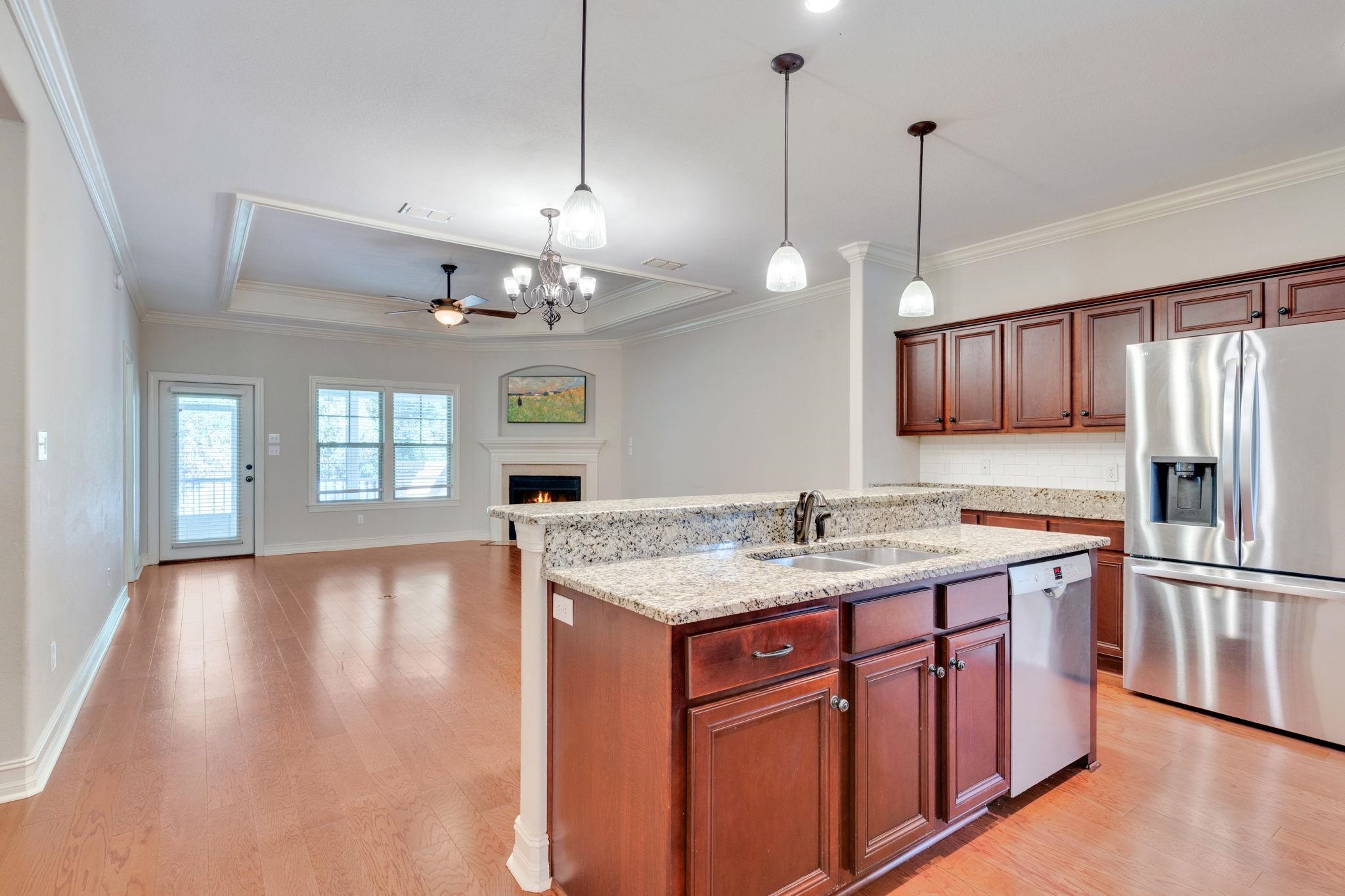Kitchen with a granite island, dark wood cabinets, stainless appliances, and an adjoining living area with a fireplace.