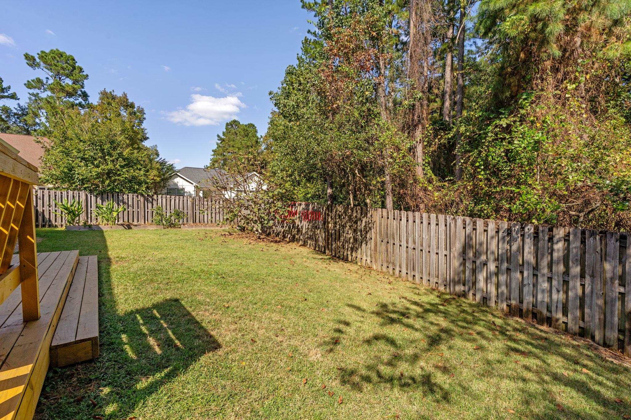 Fenced backyard with a grassy lawn, mature trees, and a wooden deck.