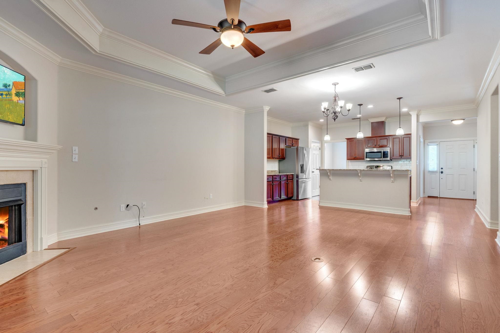 Vacant living room with hardwood floors, fireplace, and open kitchen with dark wood cabinets.