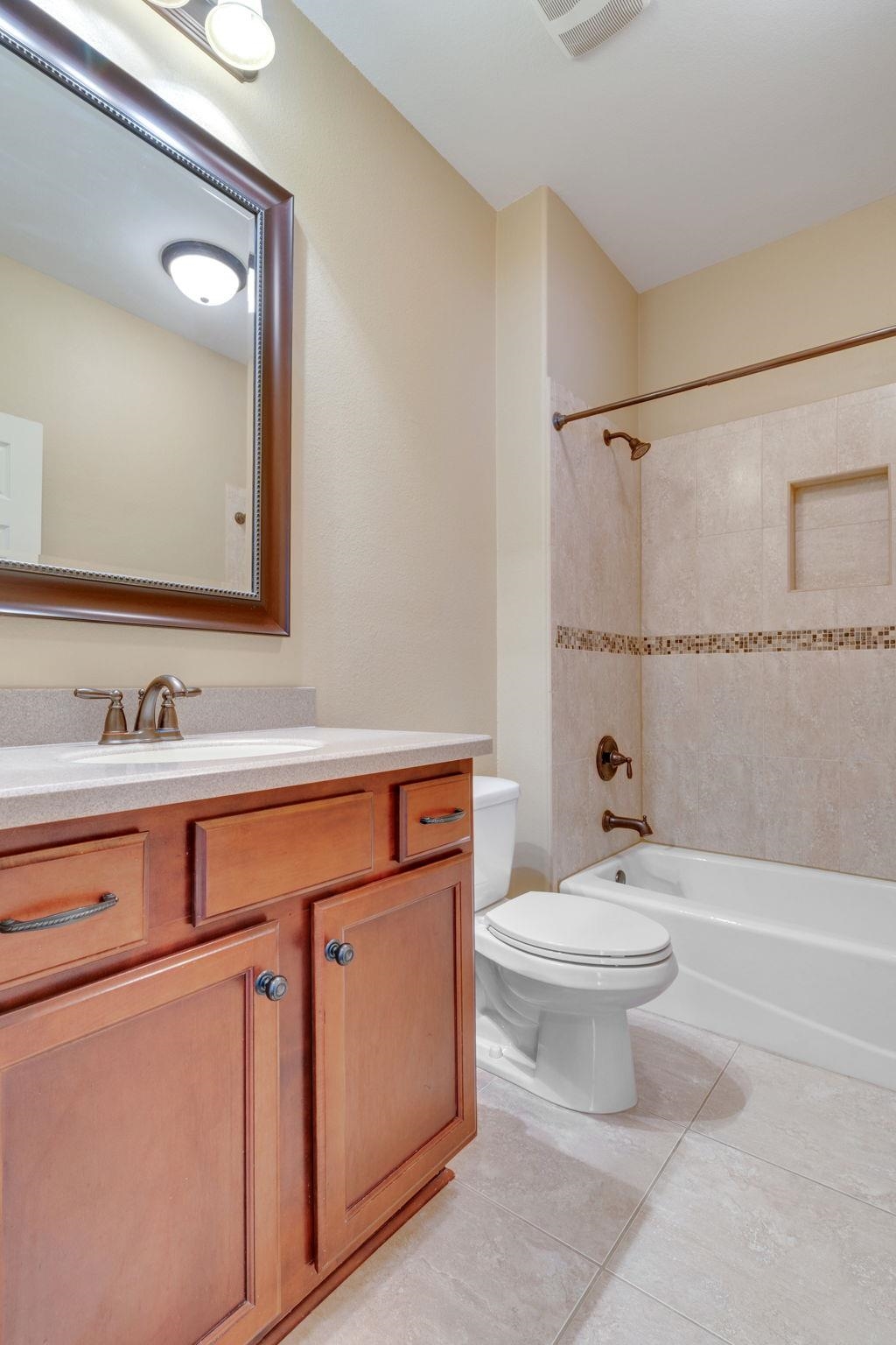 Bathroom with wood vanity, framed mirror, and tiled tub surround with mosaic accent stripe.
