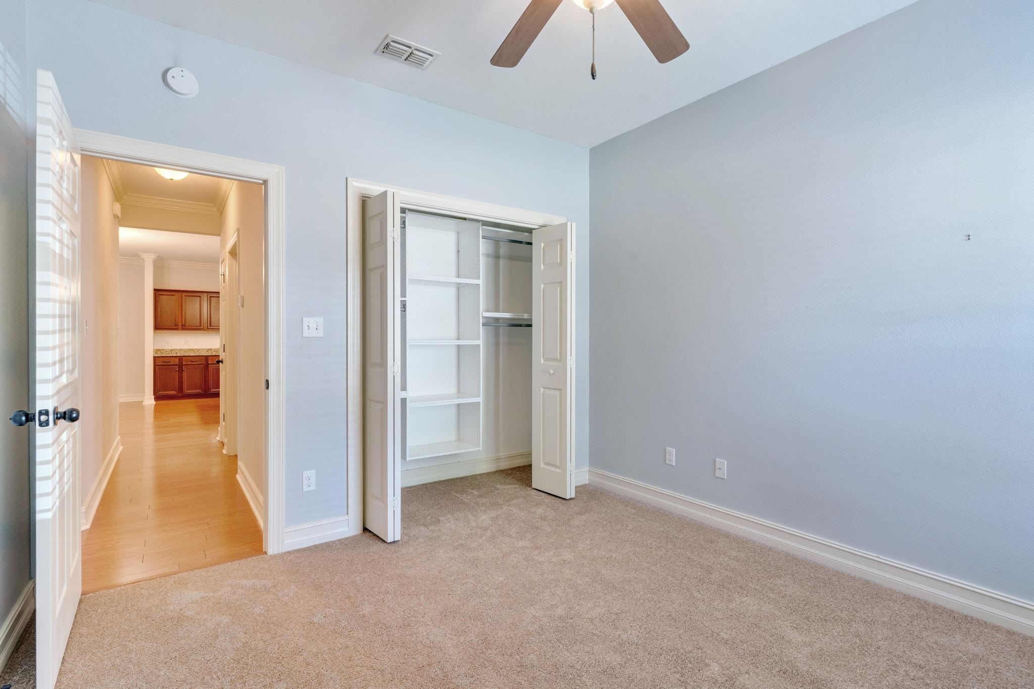 Empty carpeted bedroom with an open, built-in closet and a hallway visible through the doorway.