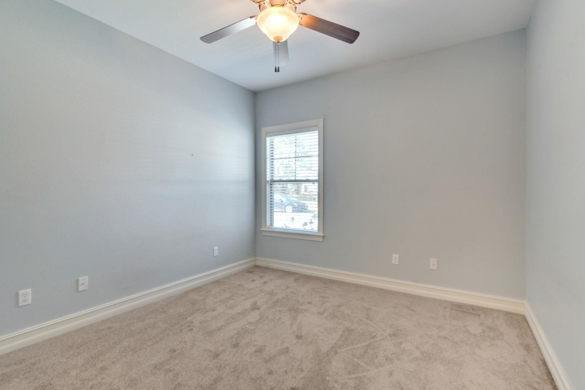 Empty carpeted room with pale blue walls, a window with blinds, and a ceiling fan.