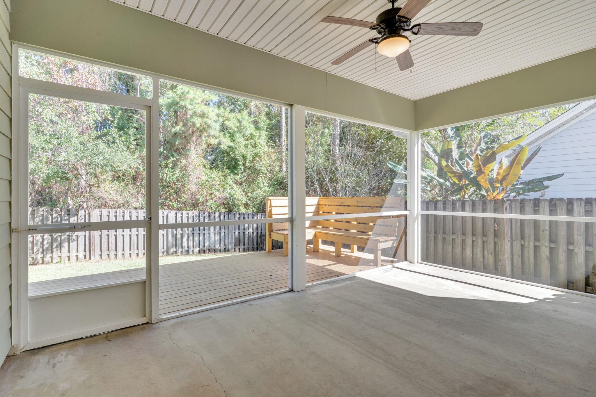 Covered screened patio with a ceiling fan, concrete floor, wooden bench, and fenced backyard.