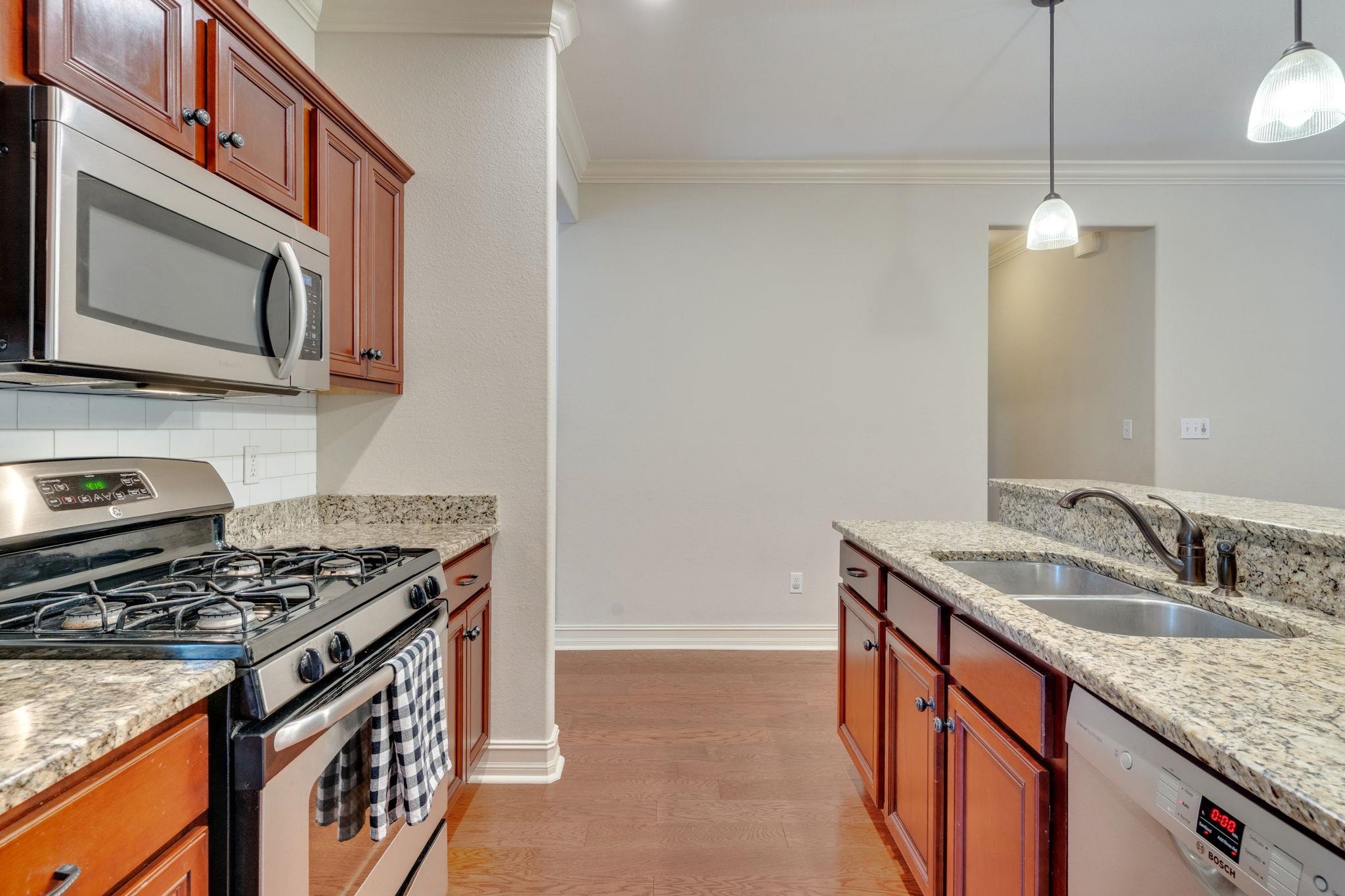 Kitchen with reddish-brown cabinets, granite counters, gas range, and double-basin sink.