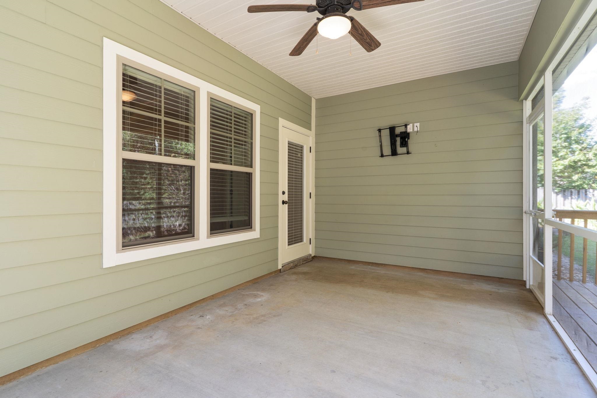 Screened porch with pale green siding, concrete floor, ceiling fan, and glass door to a deck.