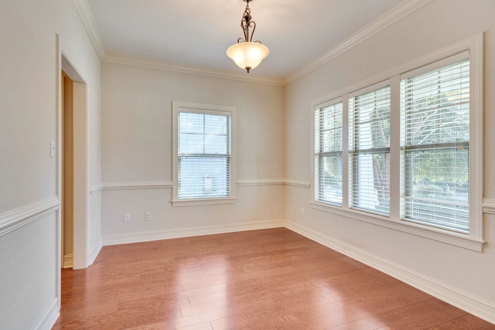Empty room with hardwood floors, a hanging light, and windows with blinds
