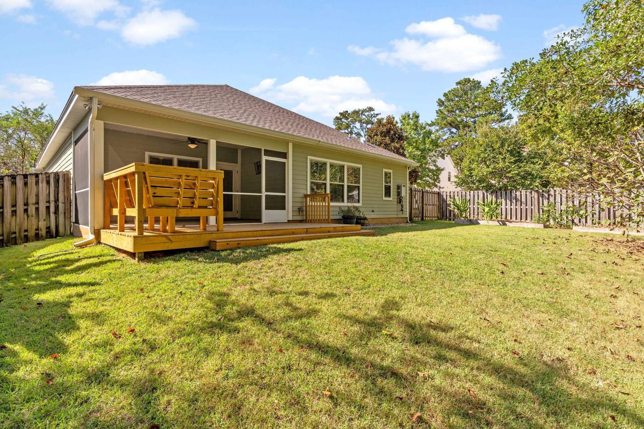 Home’s rear screened porch and raised wooden deck overlook a grassy, fenced backyard.