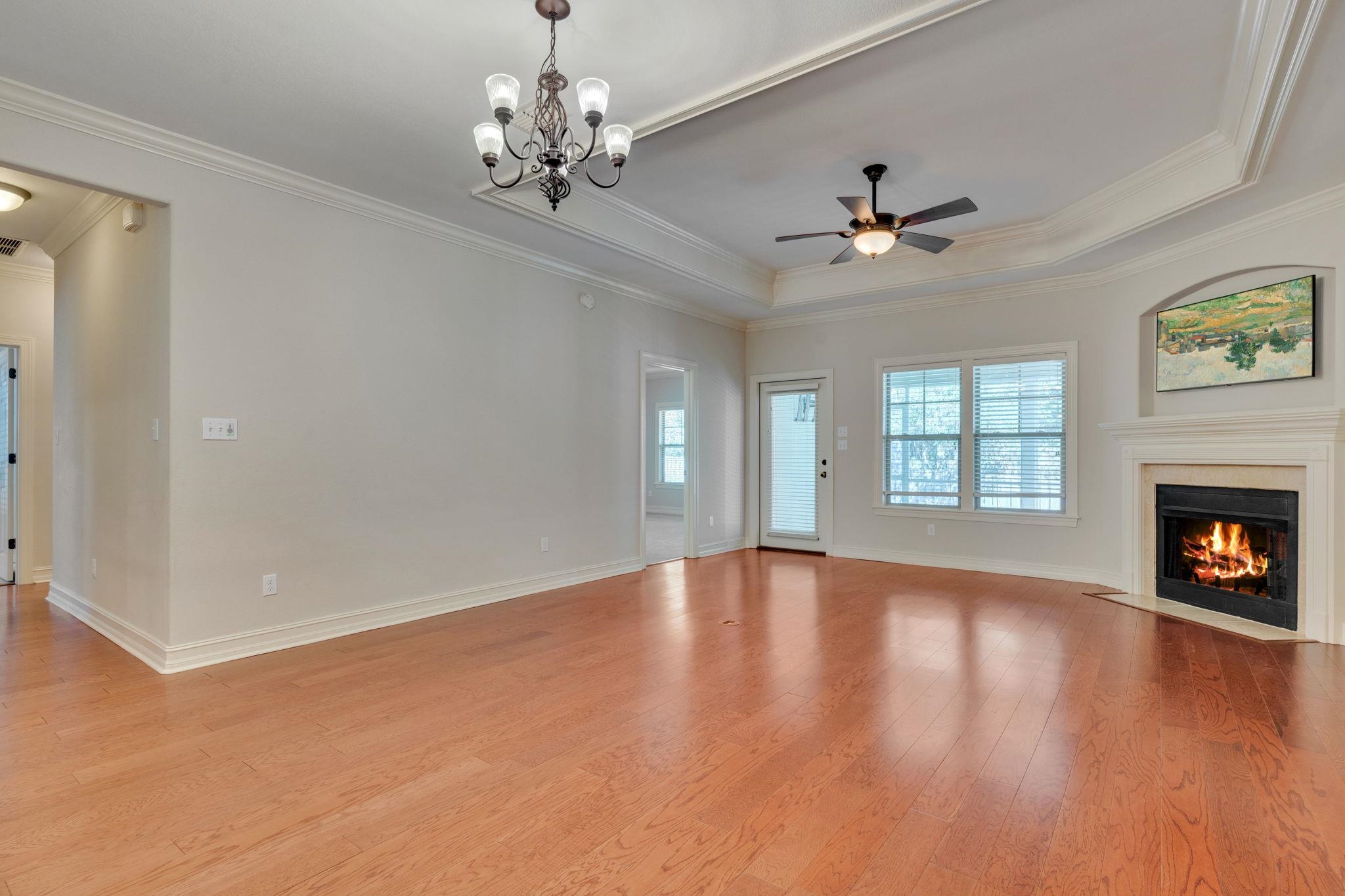 Vacant living room with hardwood floors, a fireplace, and a tray ceiling.