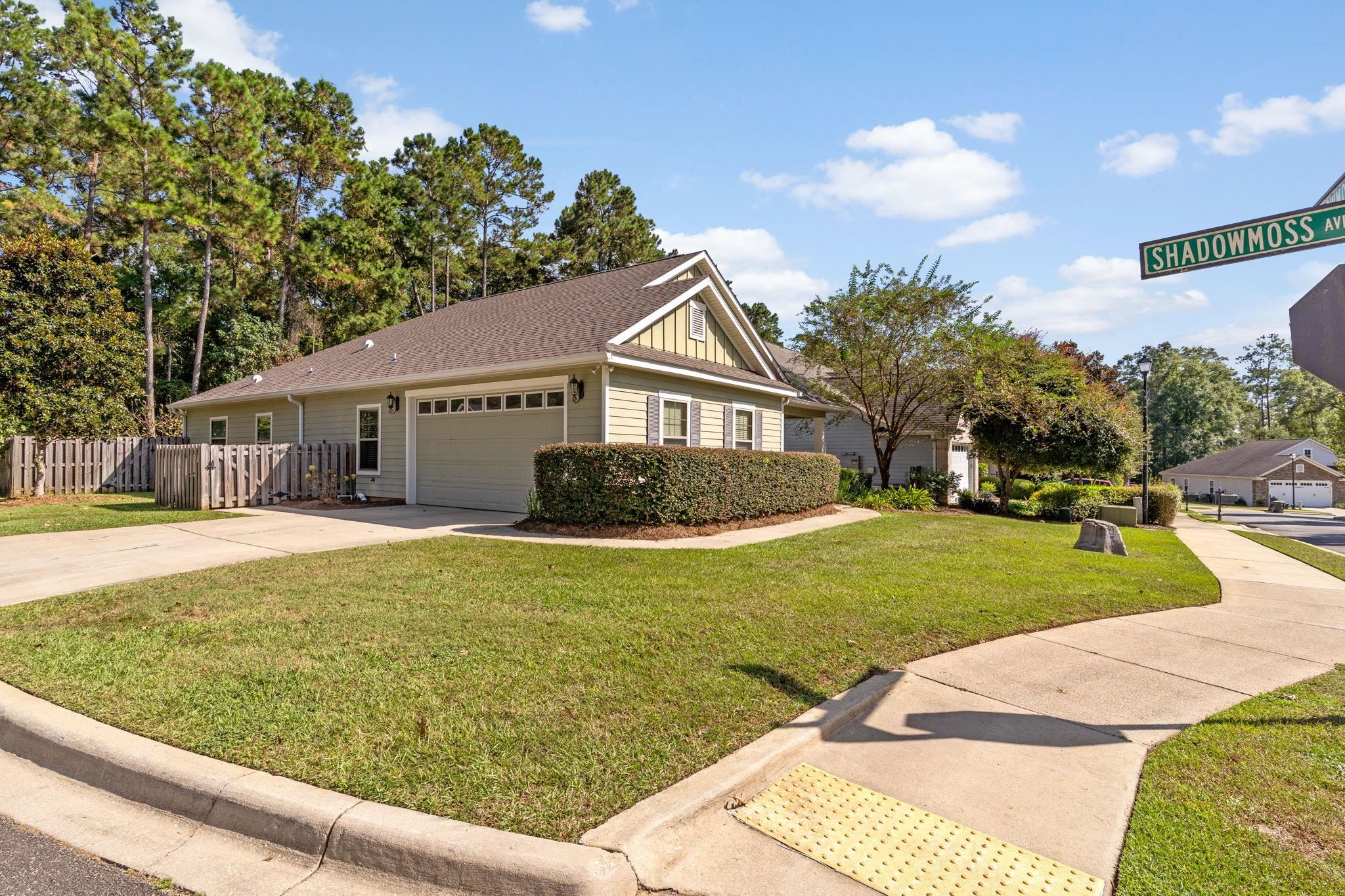 Gray single-story home with an attached garage, trimmed hedges, and a Shadowmoss Ave street sign.