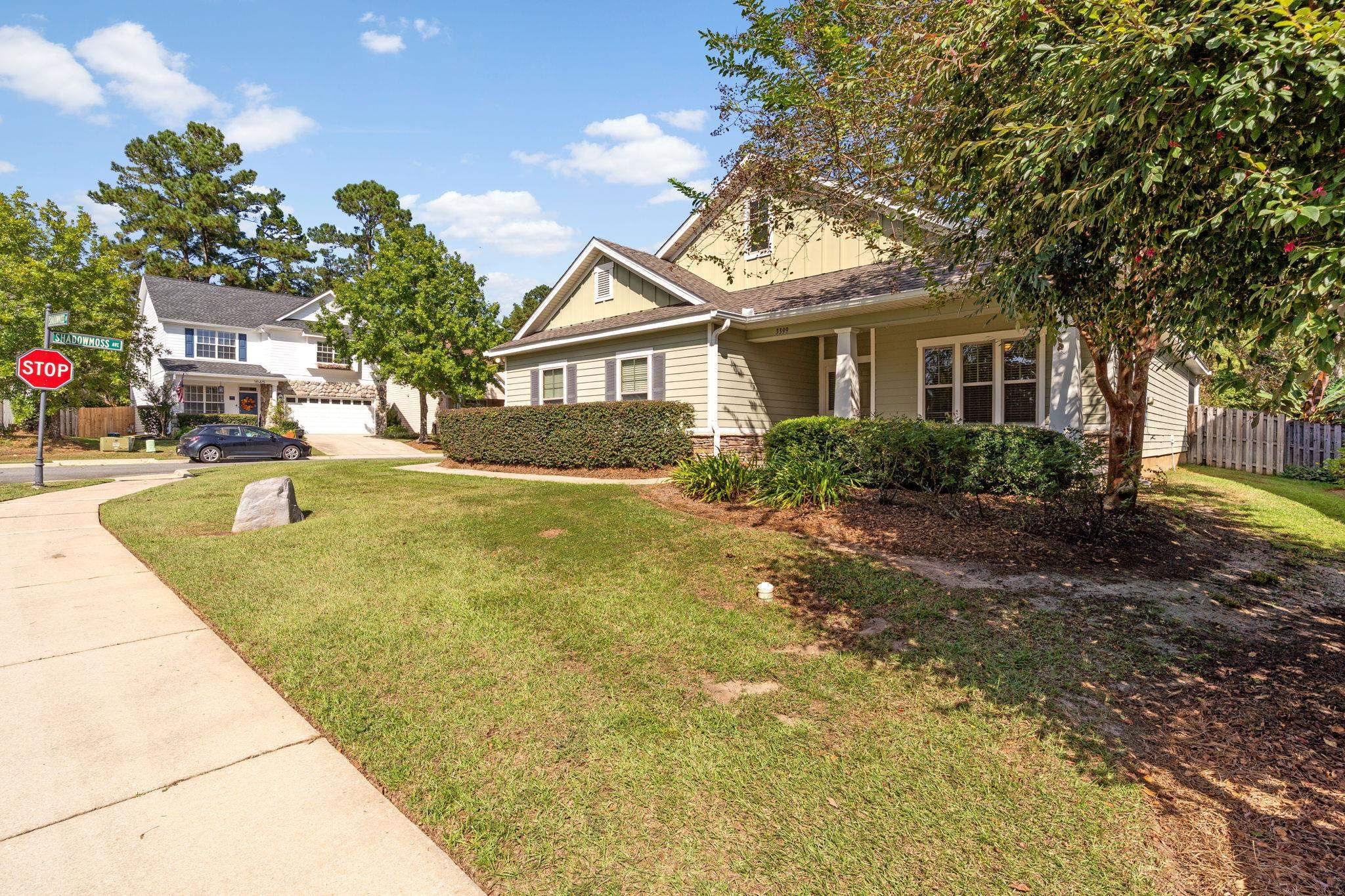 Tan-sided home with a covered porch, broad lawn, mature trees, and Shadowmoss Avenue street sign.
