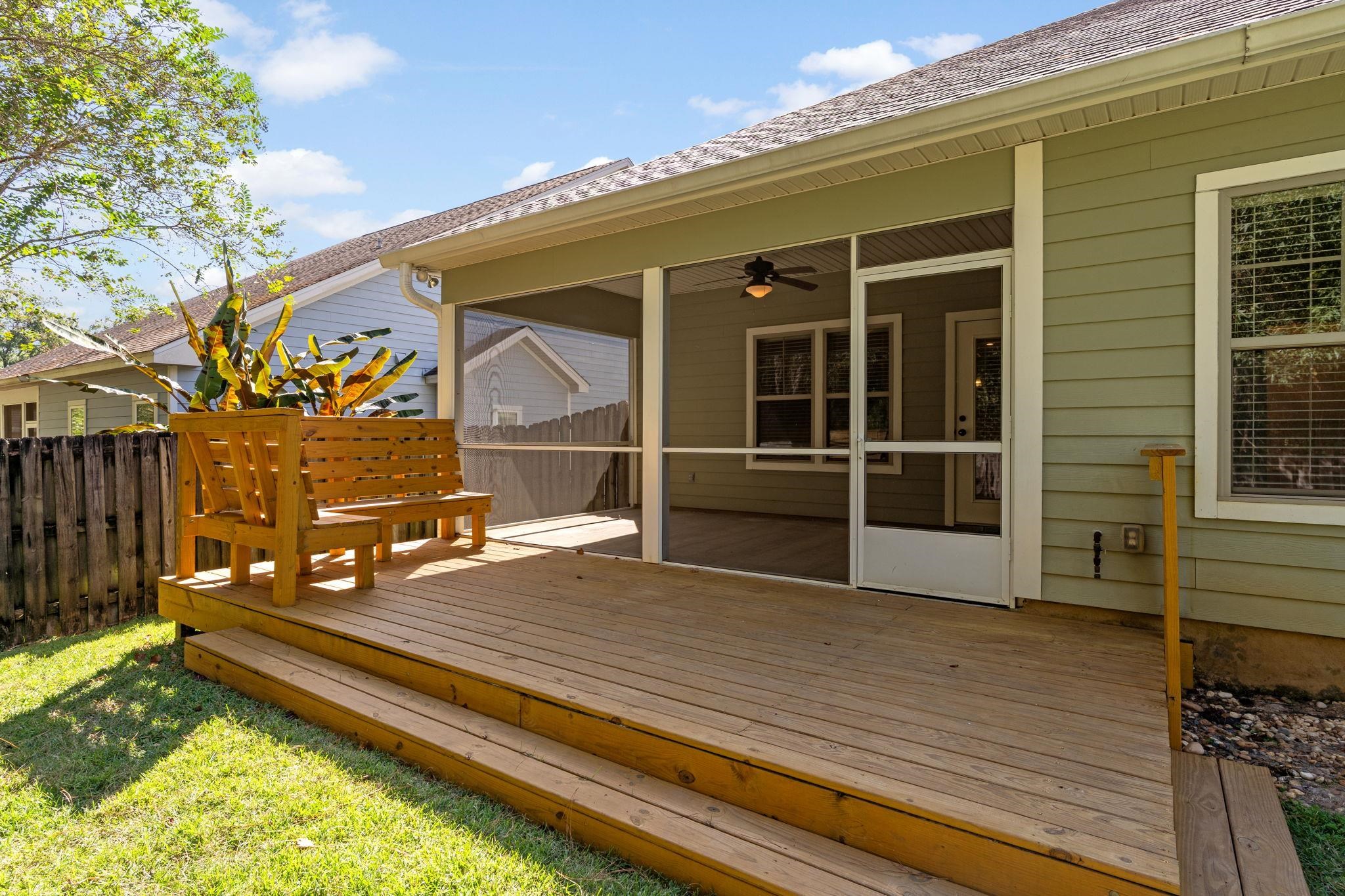 Wooden deck with bench and plants beside a screened porch at the rear of a home.