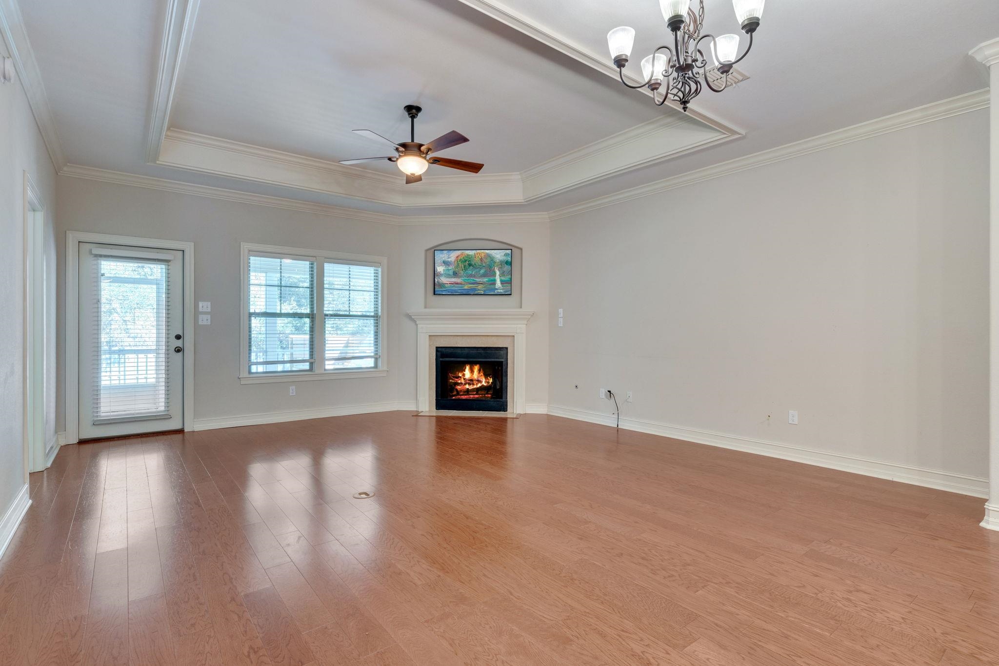 Empty living room with hardwood floors, a lit corner fireplace, and a tray ceiling.