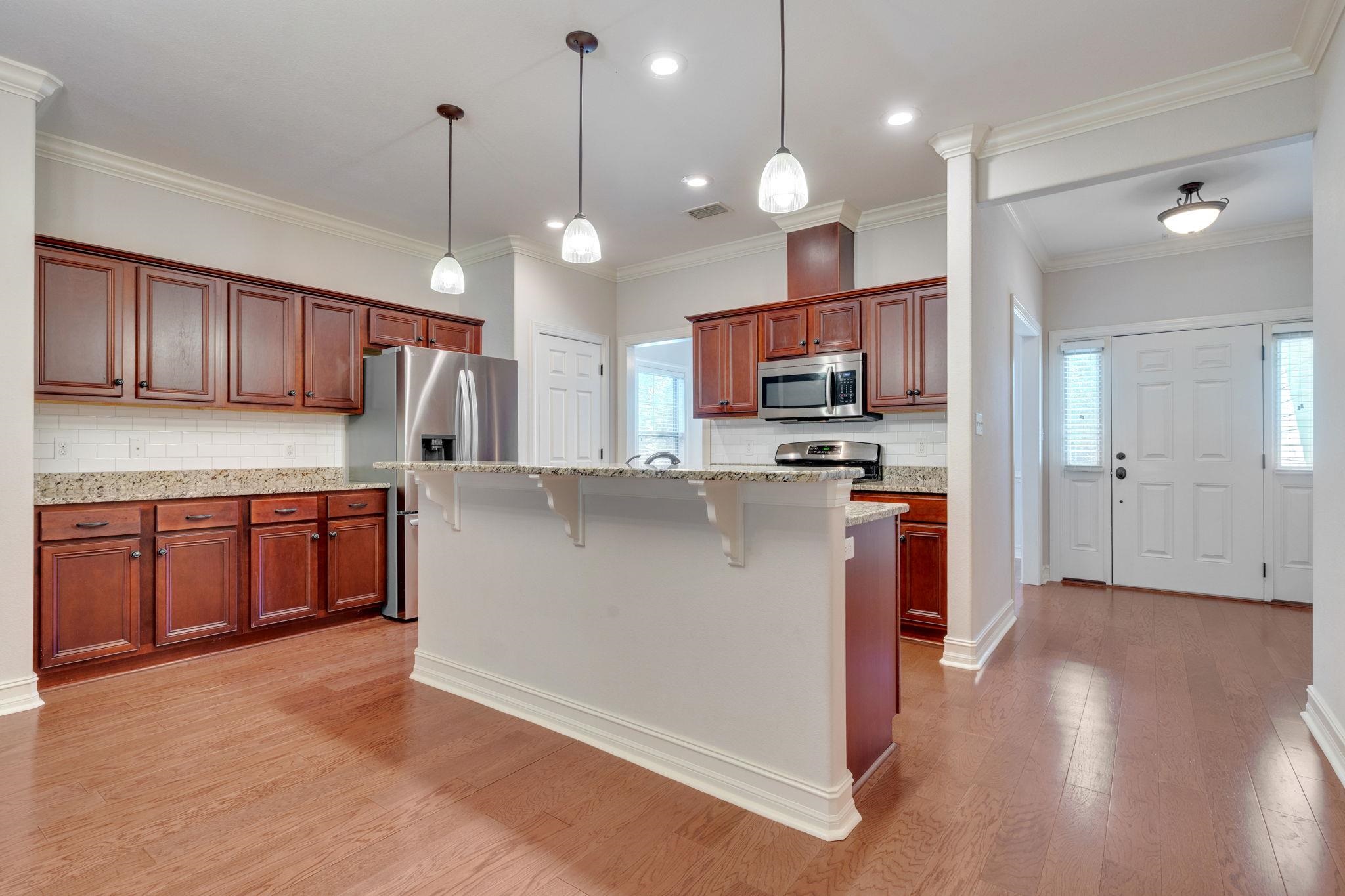 Kitchen with reddish wood cabinets, stainless steel appliances, and a granite-topped island beside the front entry.