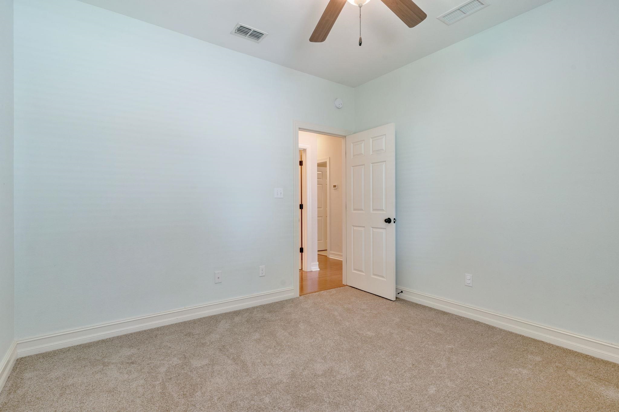 Empty bedroom with pale blue walls, beige carpet, and an open door to the hallway.