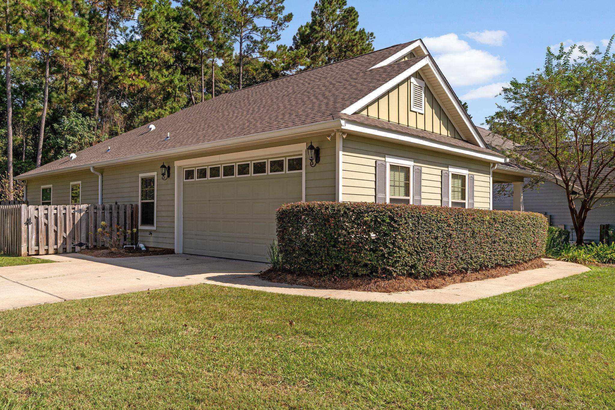 Beige house with a two-car garage, long trimmed hedge, and concrete driveway.
