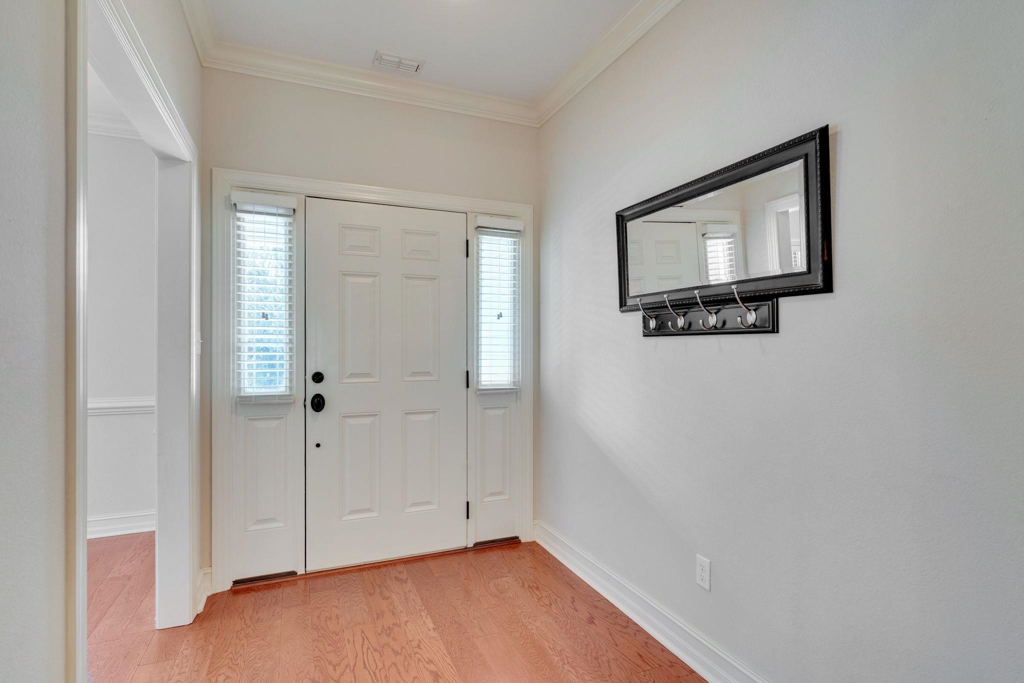 Entry foyer with a white paneled front door, sidelights, wood flooring, and a mirror with coat hooks.