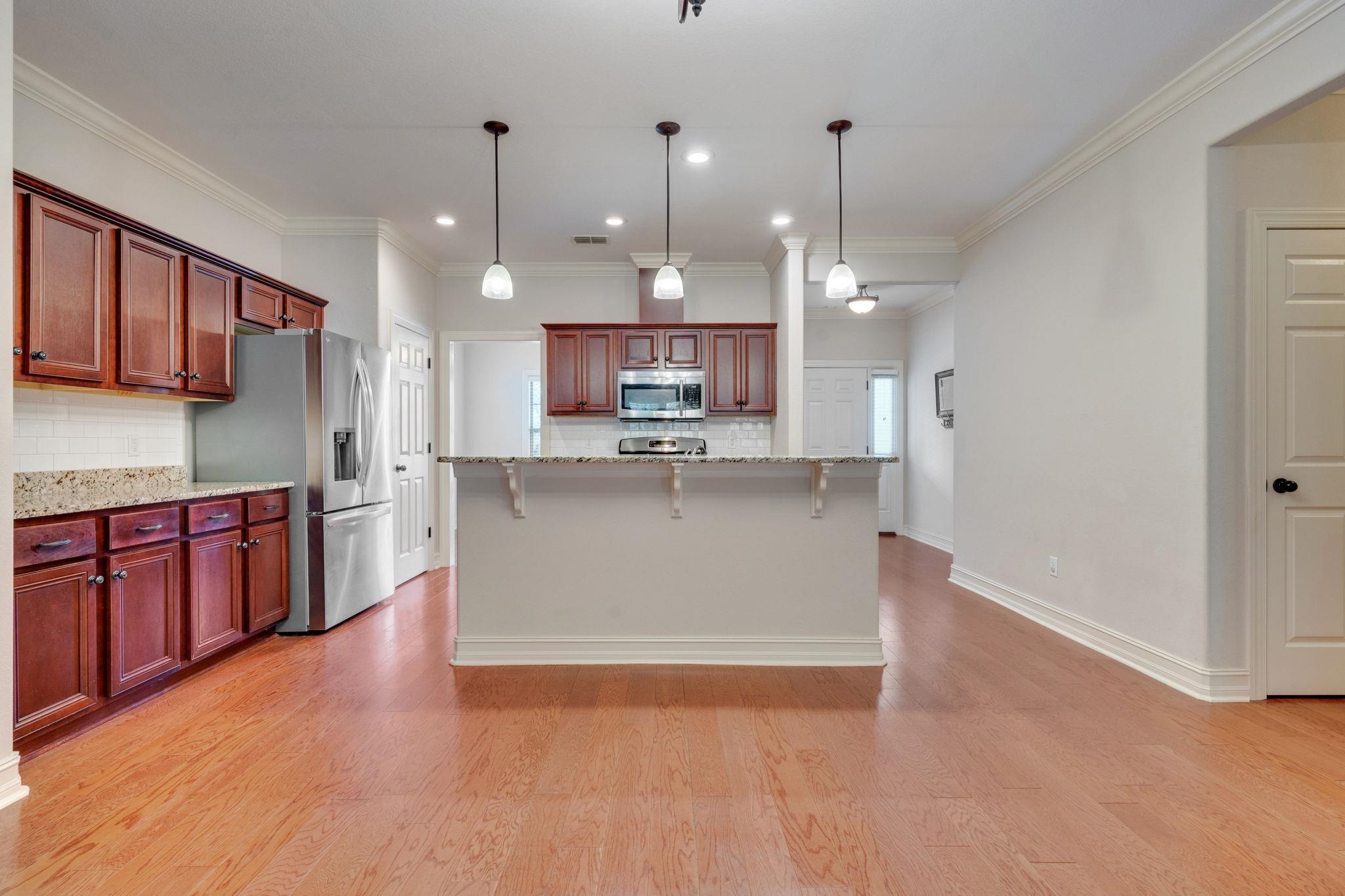 Kitchen with reddish-brown wood cabinets, stainless steel appliances, a large island, and hardwood floors.