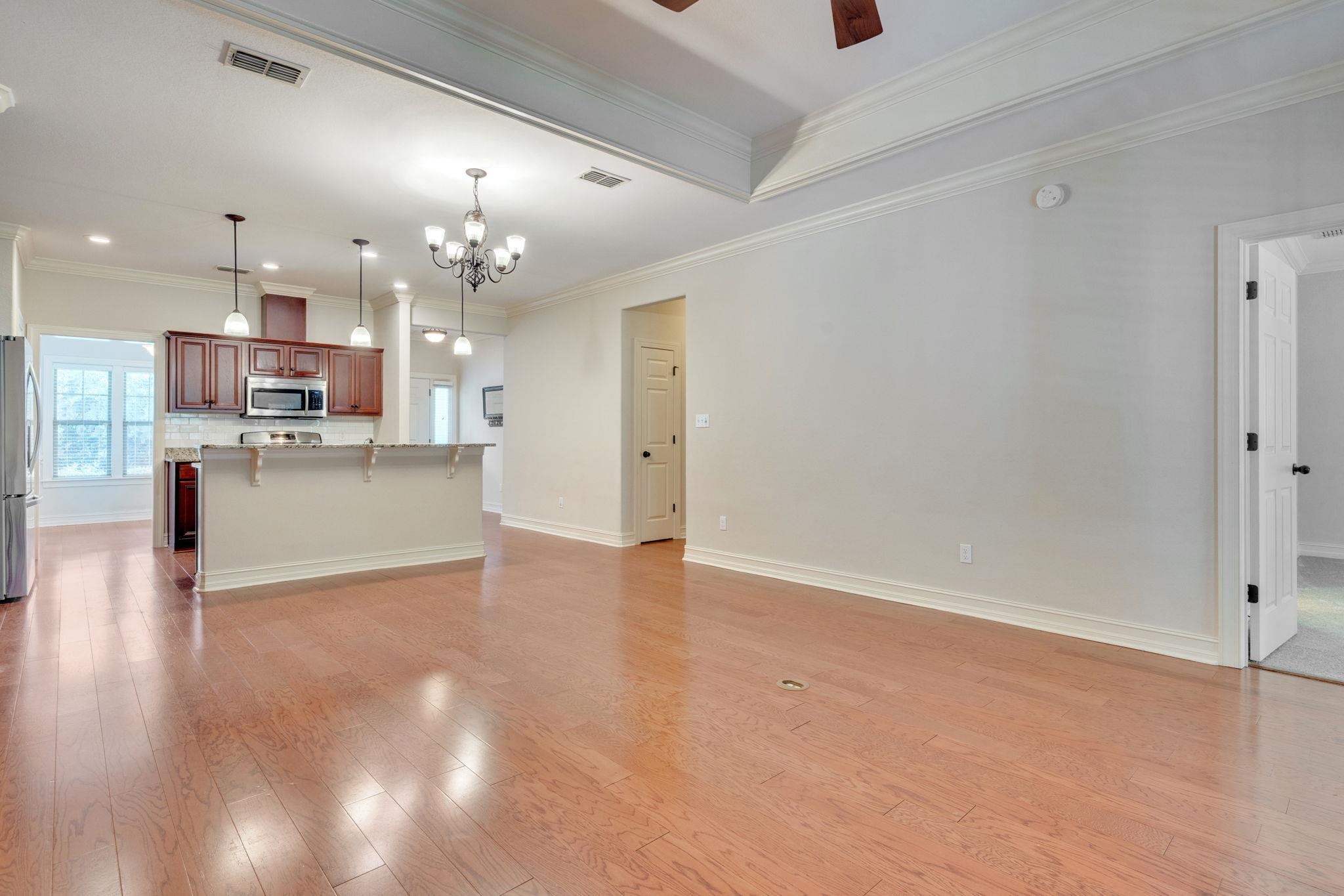 Open dining and living area with wood floors, tray ceiling, and adjoining kitchen with breakfast bar.