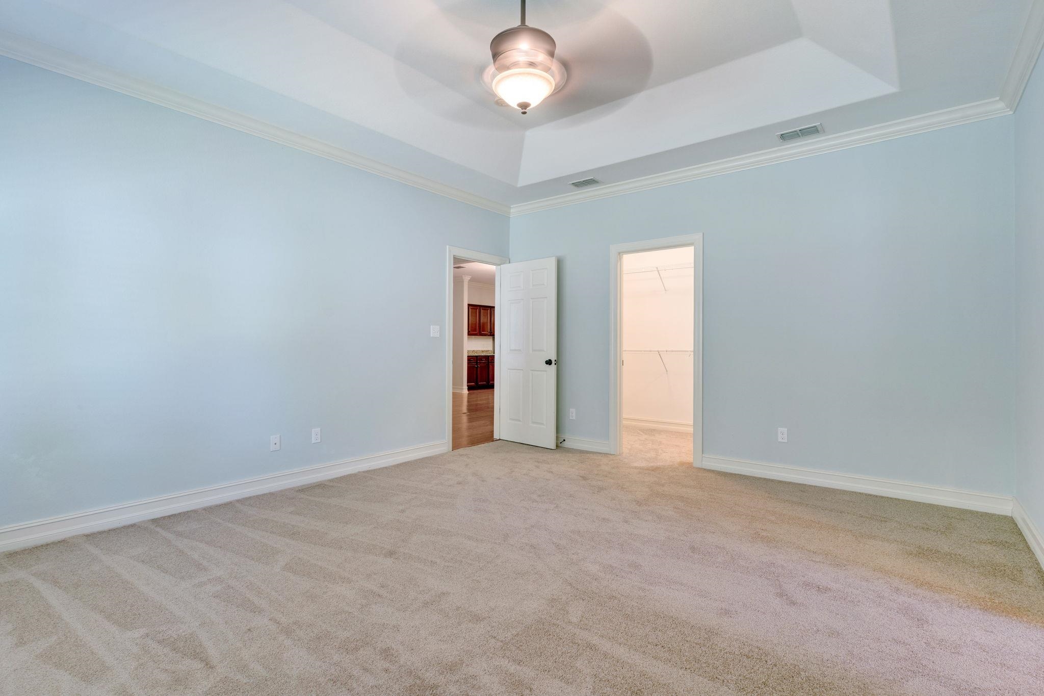 Empty bedroom with beige carpet, pale blue walls, and a tray ceiling.