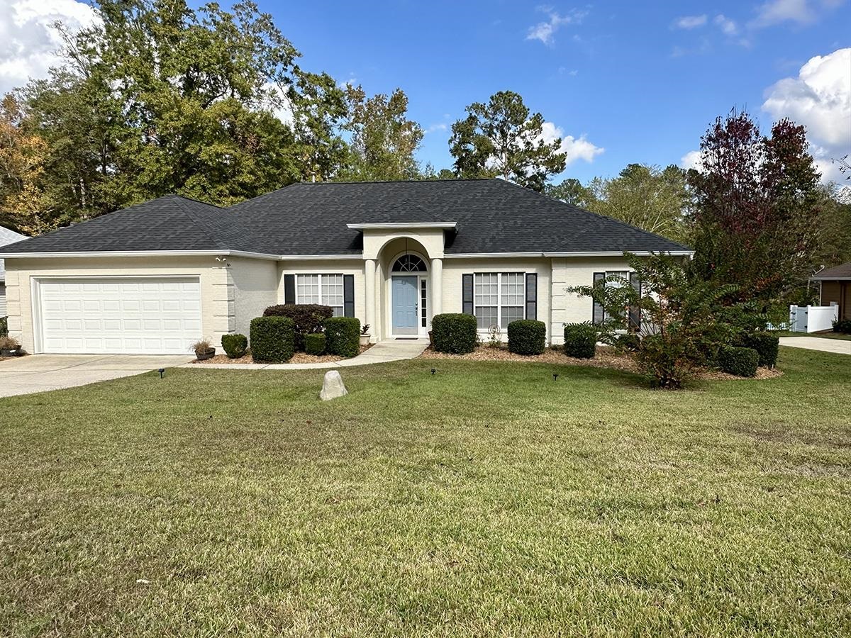 Single-story brick home with an arched entry, blue door, attached garage, and broad front lawn.