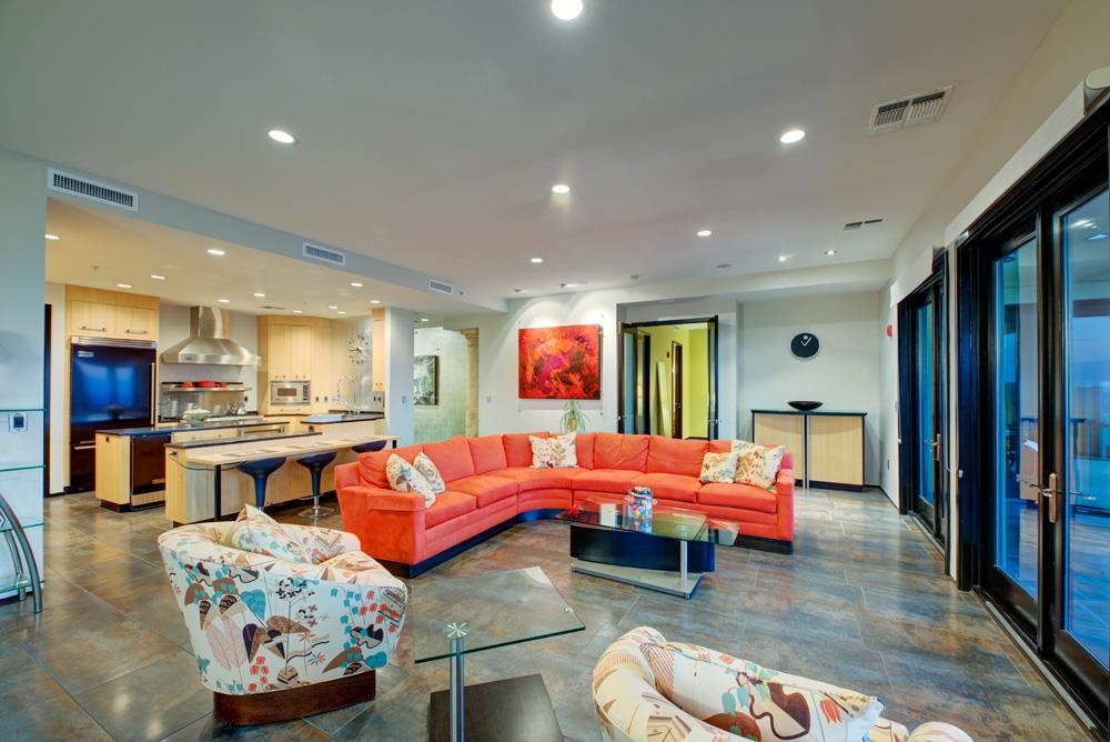 Open-plan living room with a coral sectional, patterned armchairs, kitchen island, and large glass doors.