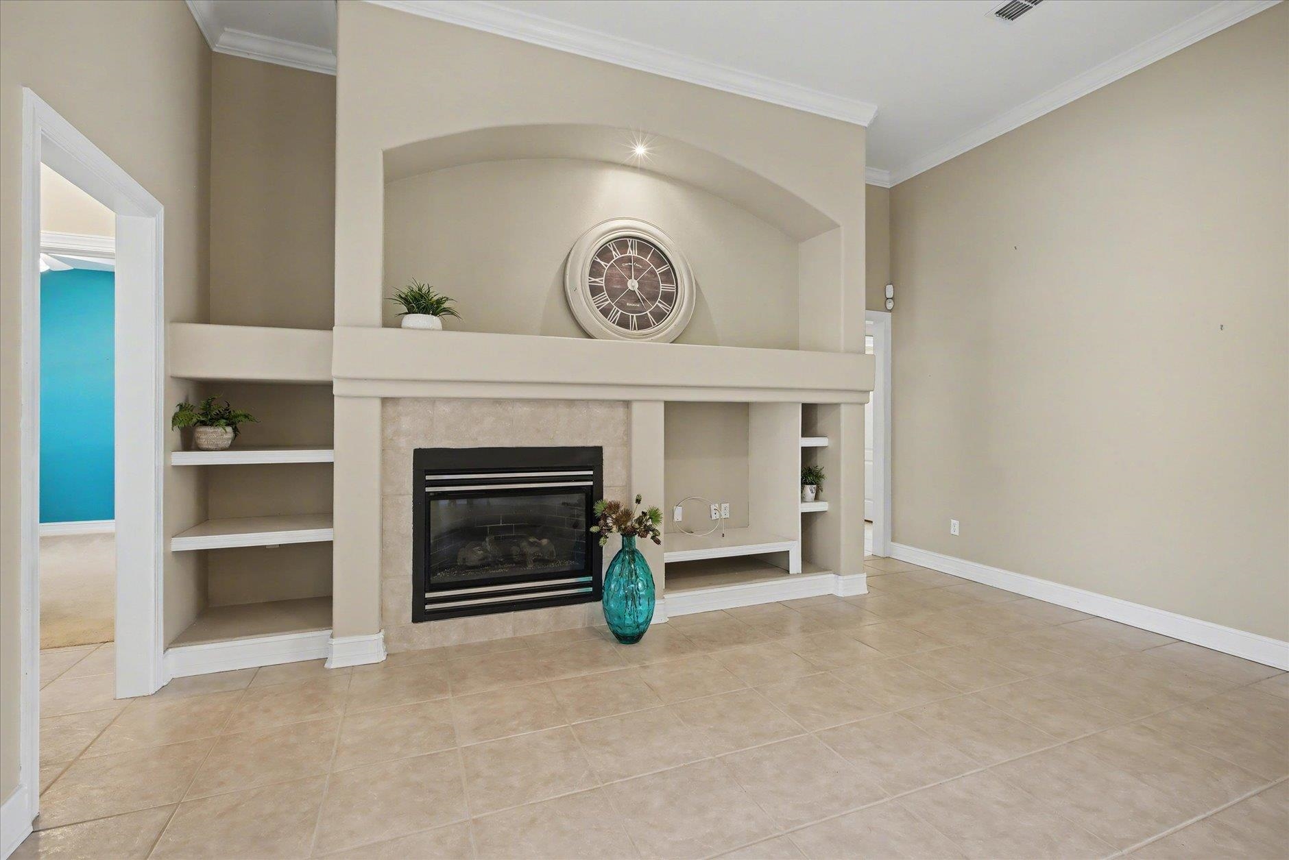 Living room fireplace with built-in shelves, a large round clock, and a turquoise vase.