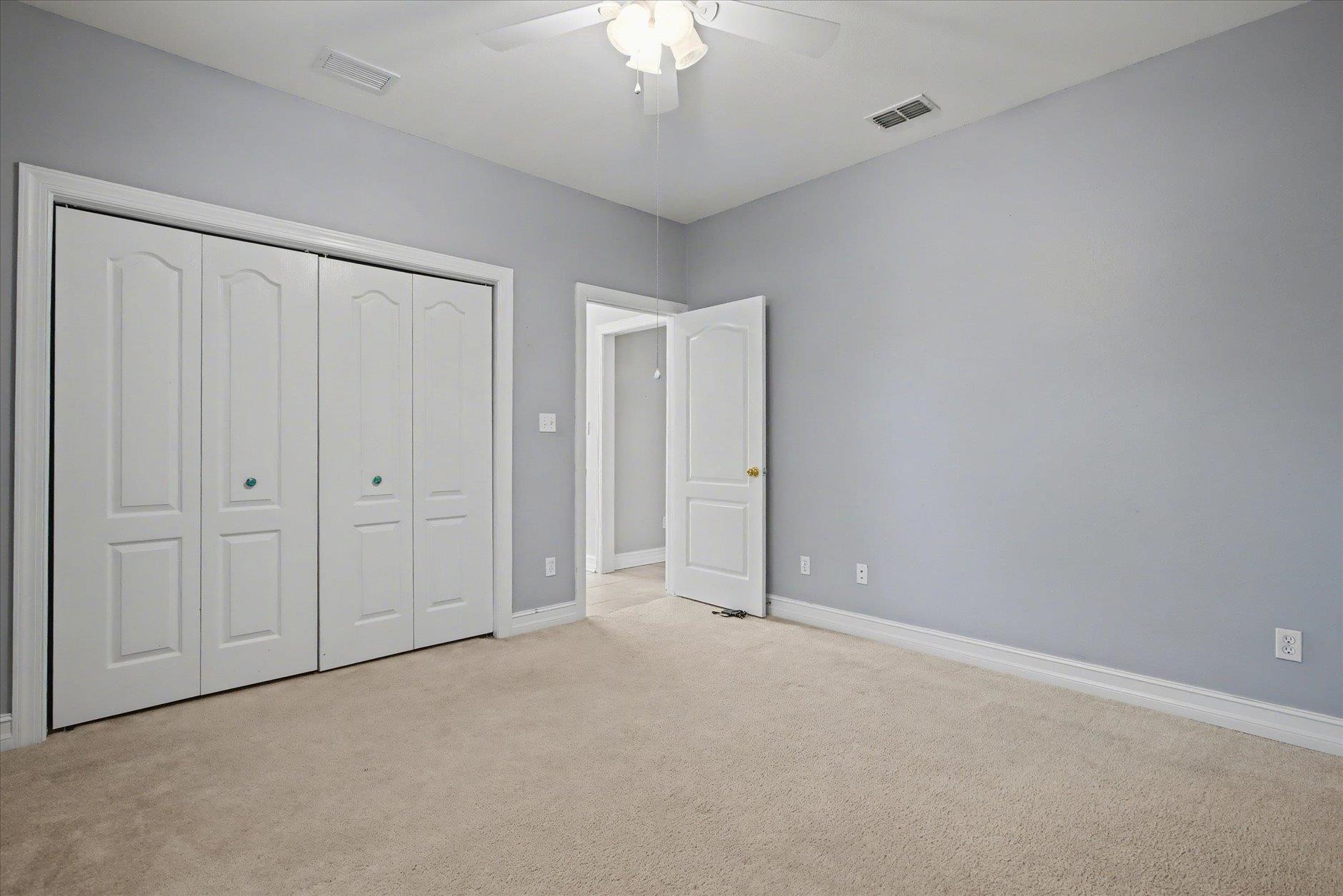 Empty bedroom with beige carpet, white closet doors, and an open door to a tiled hallway.