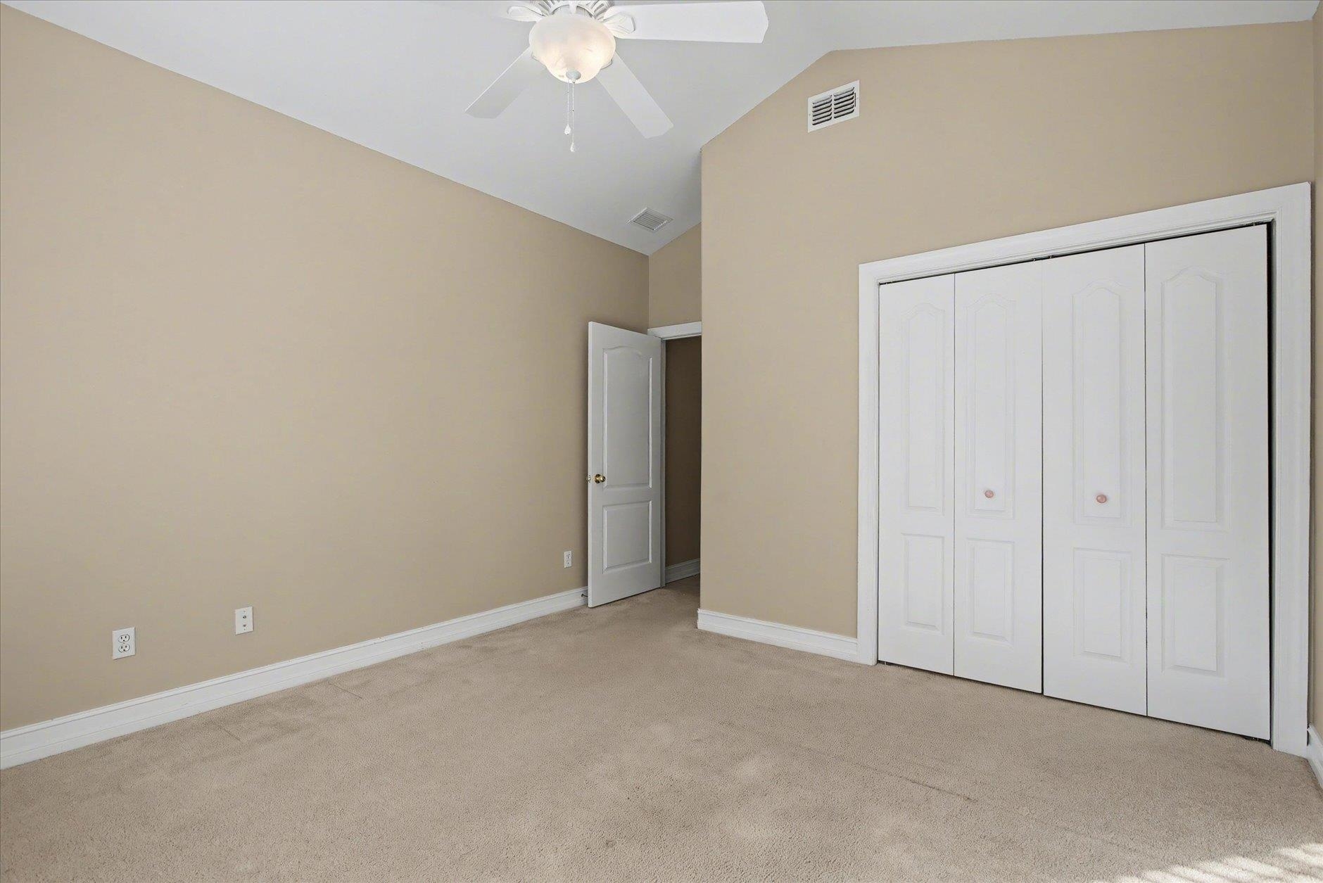 Empty carpeted bedroom with a ceiling fan, four-panel closet, and open doorway.