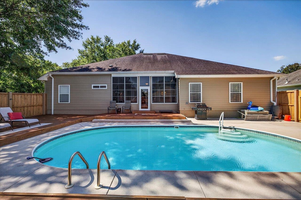 Home’s rear exterior and fenced backyard, with a curved swimming pool and raised wood patio.