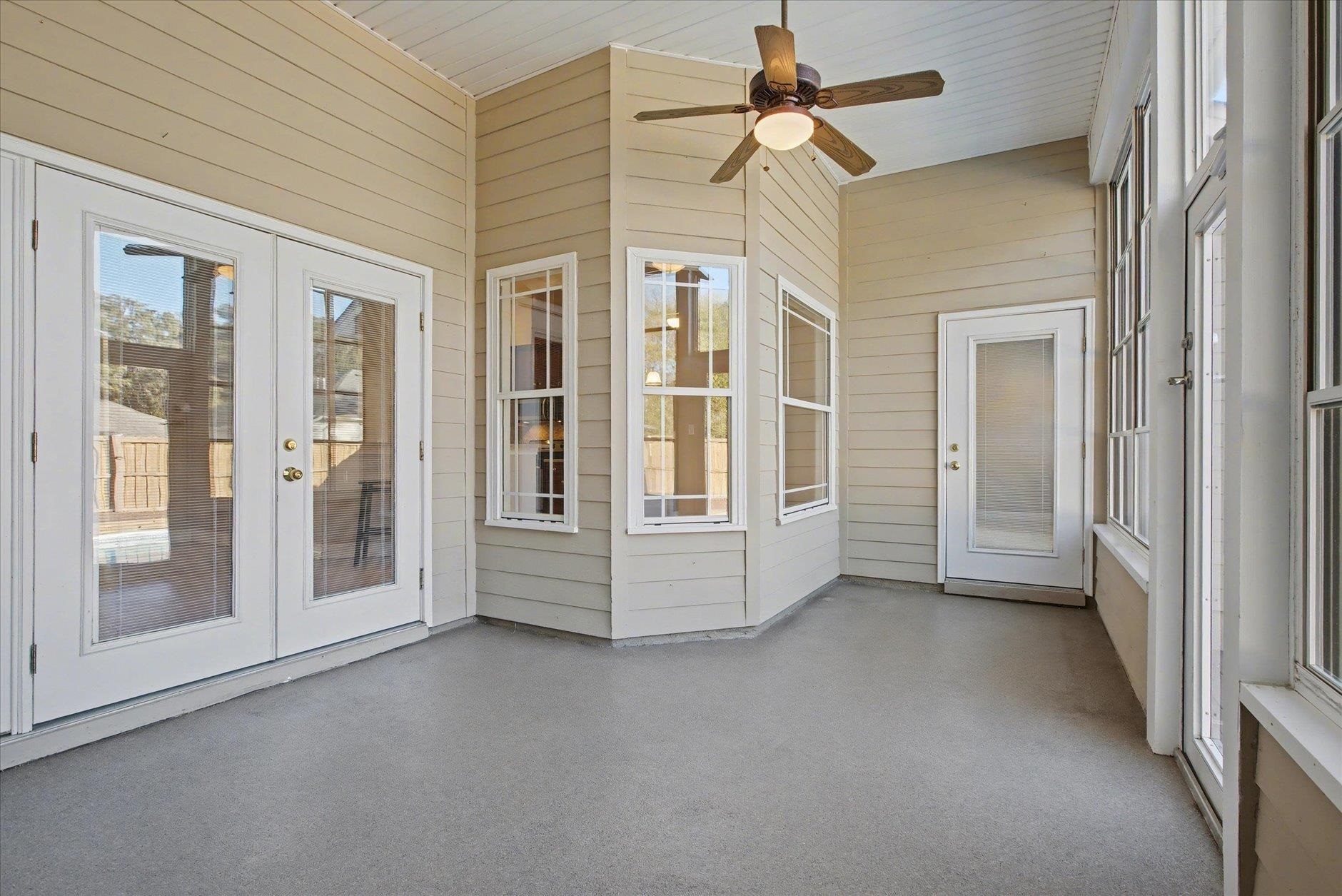 Enclosed sunroom with white-framed windows, multiple doors, and a ceiling fan.