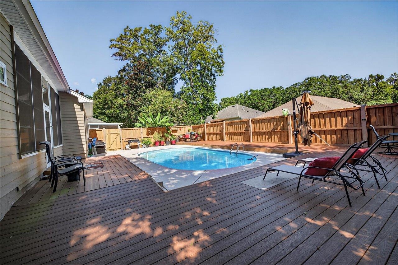 Backyard pool with a wide wooden deck, patio chairs, and a wooden privacy fence.