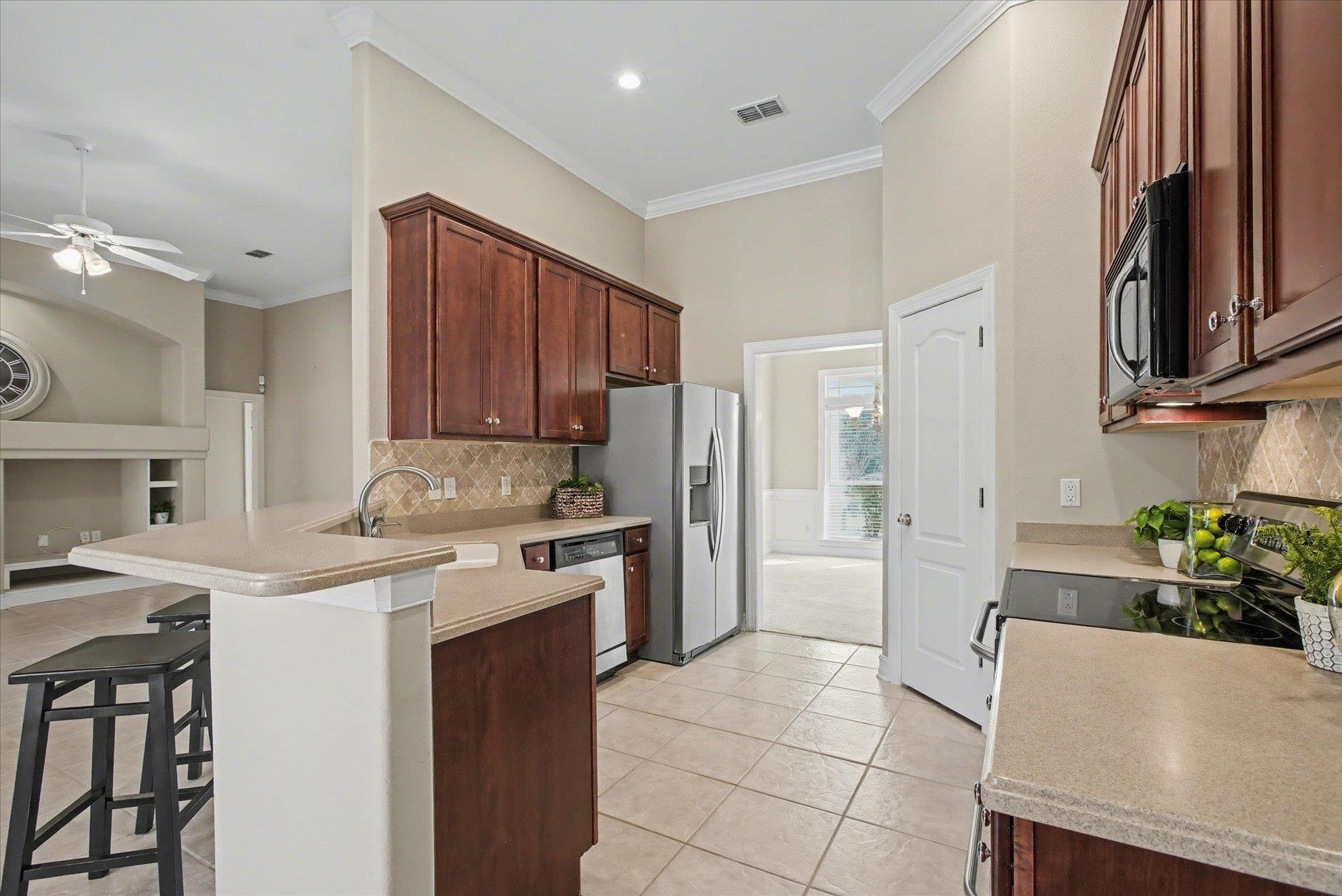 Kitchen with dark wood cabinets, stainless steel appliances, and a breakfast bar with black stools.