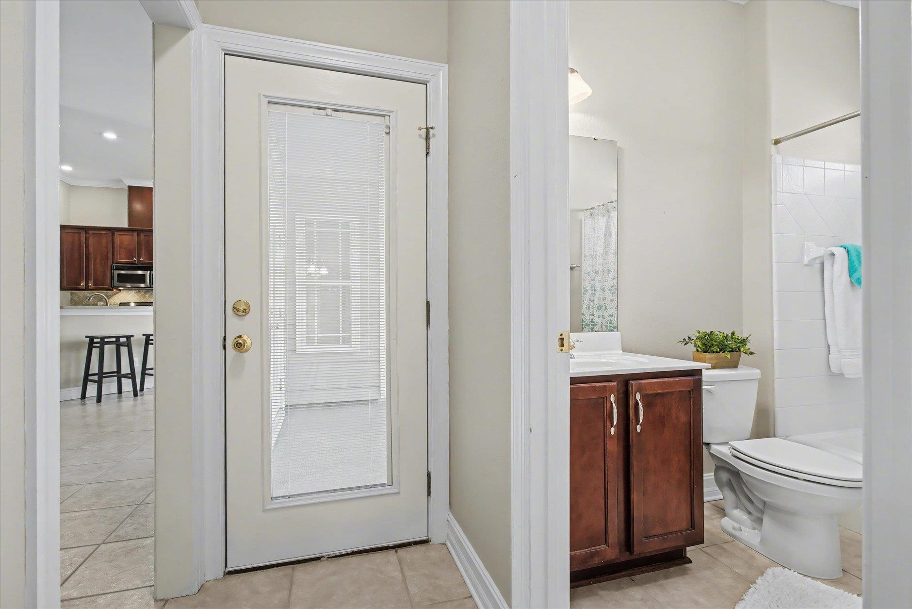 Bathroom with dark wood vanity and tiled tub and shower, viewed past a glass-panel door.