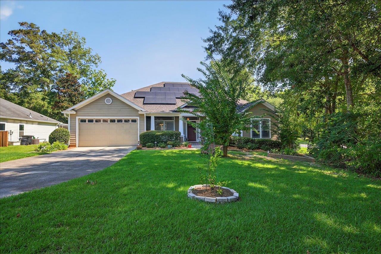 Single-story home with rooftop solar panels, a two-car garage, and a tree-lined lawn.