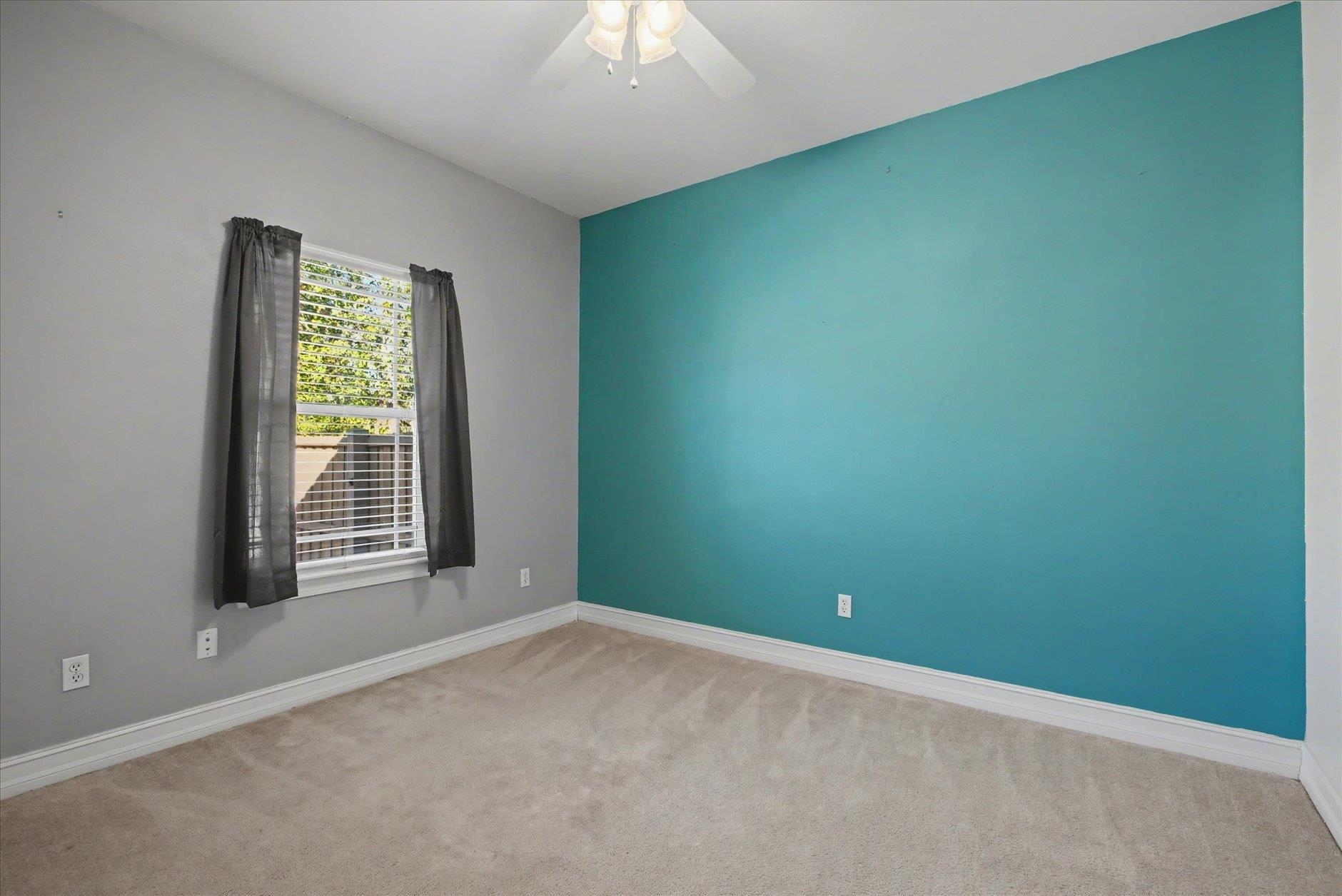 Empty bedroom with a turquoise accent wall, carpet, and a curtained window.
