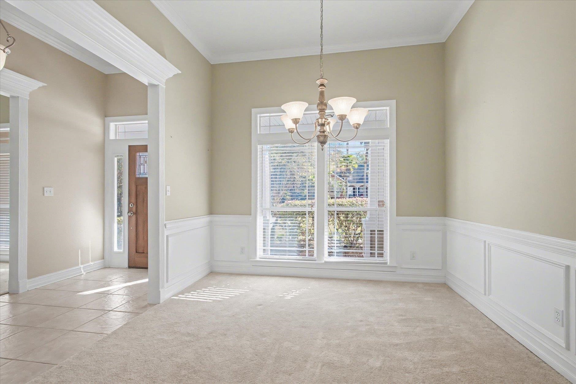 Empty dining room with a chandelier, paneled wainscoting, and a large window with blinds.