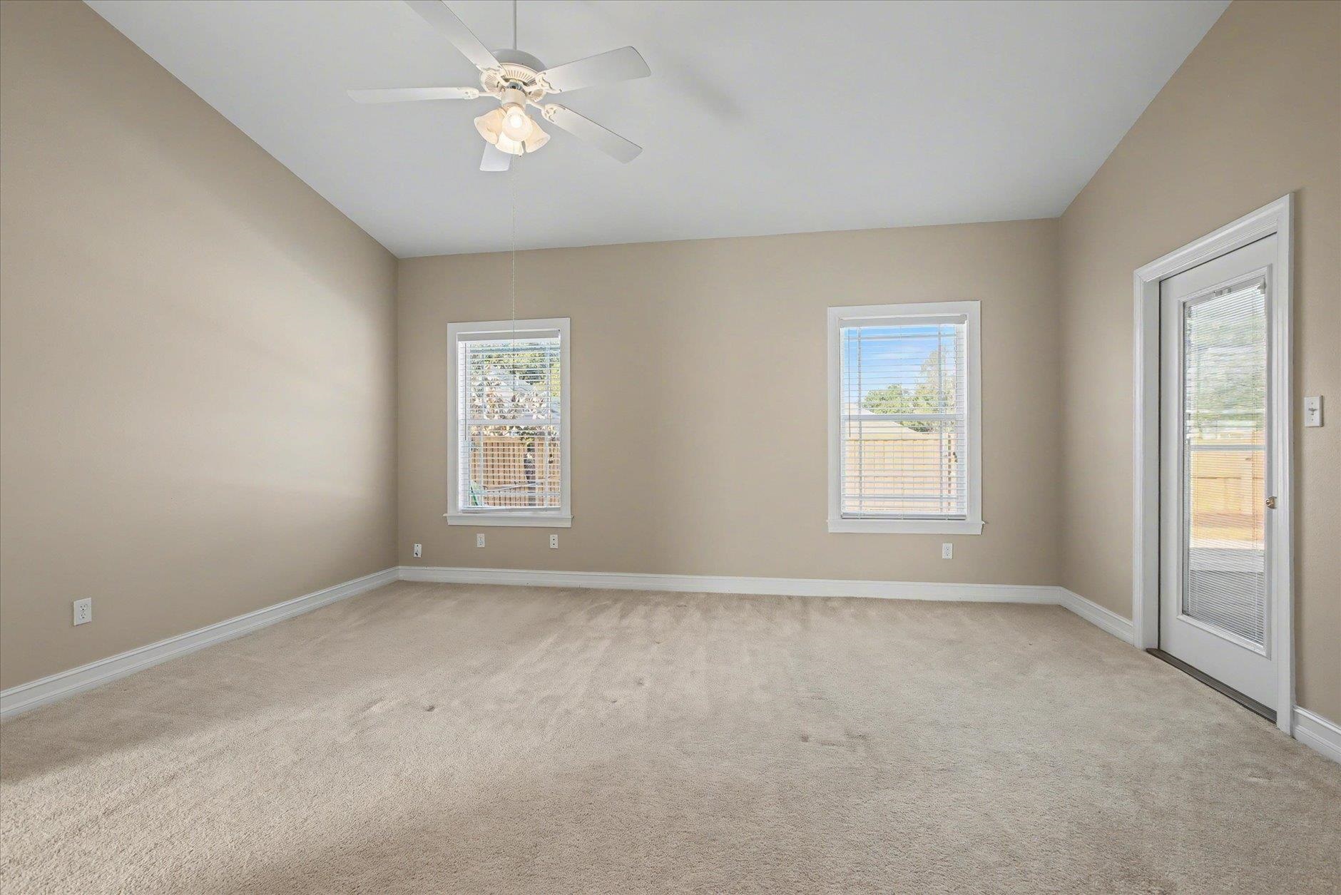 Empty carpeted room with a ceiling fan, two windows, and a glass exterior door.