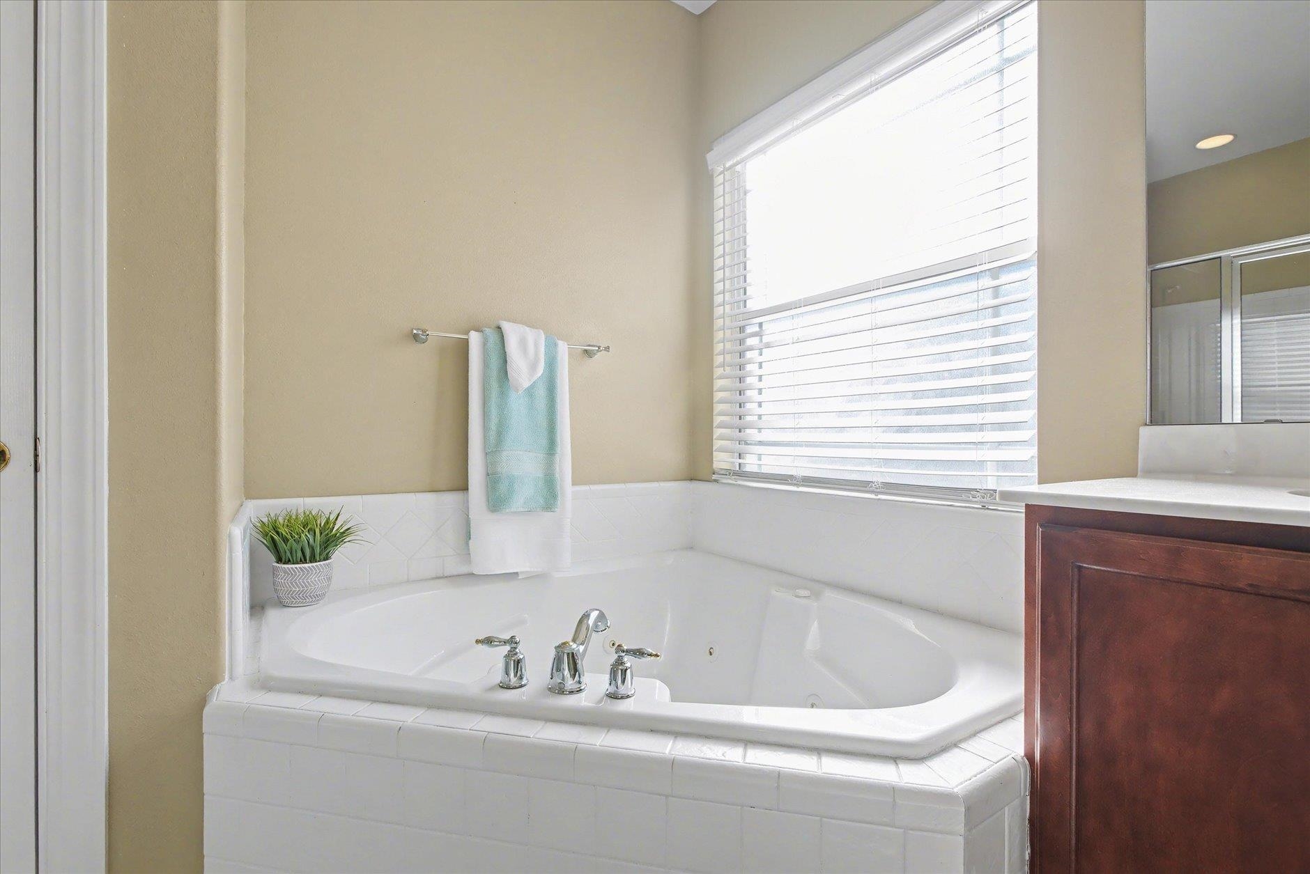Bathroom with a white jetted soaking tub beneath a bright window with blinds.