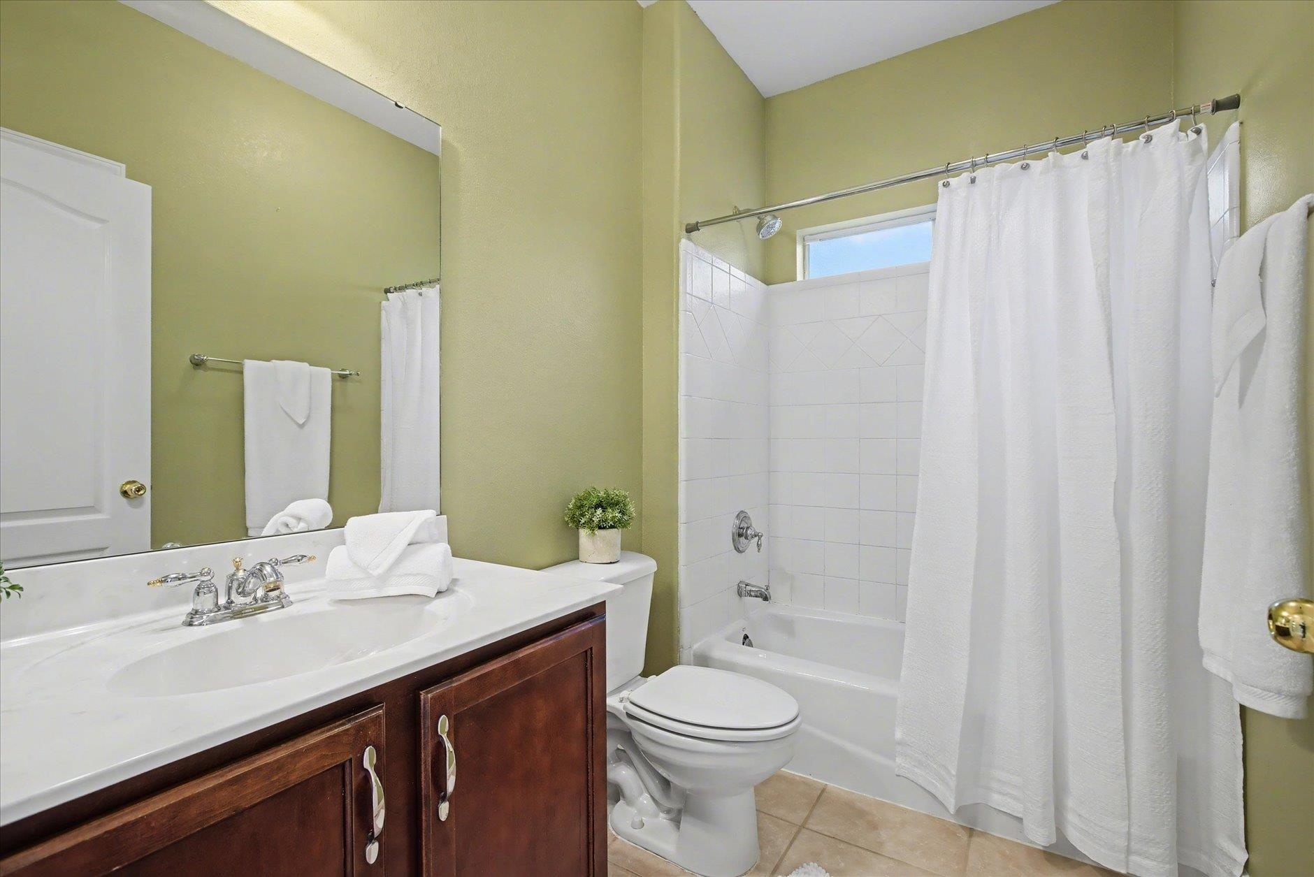 Bathroom with a dark wood vanity, large mirror, and white-curtained tiled tub and shower.