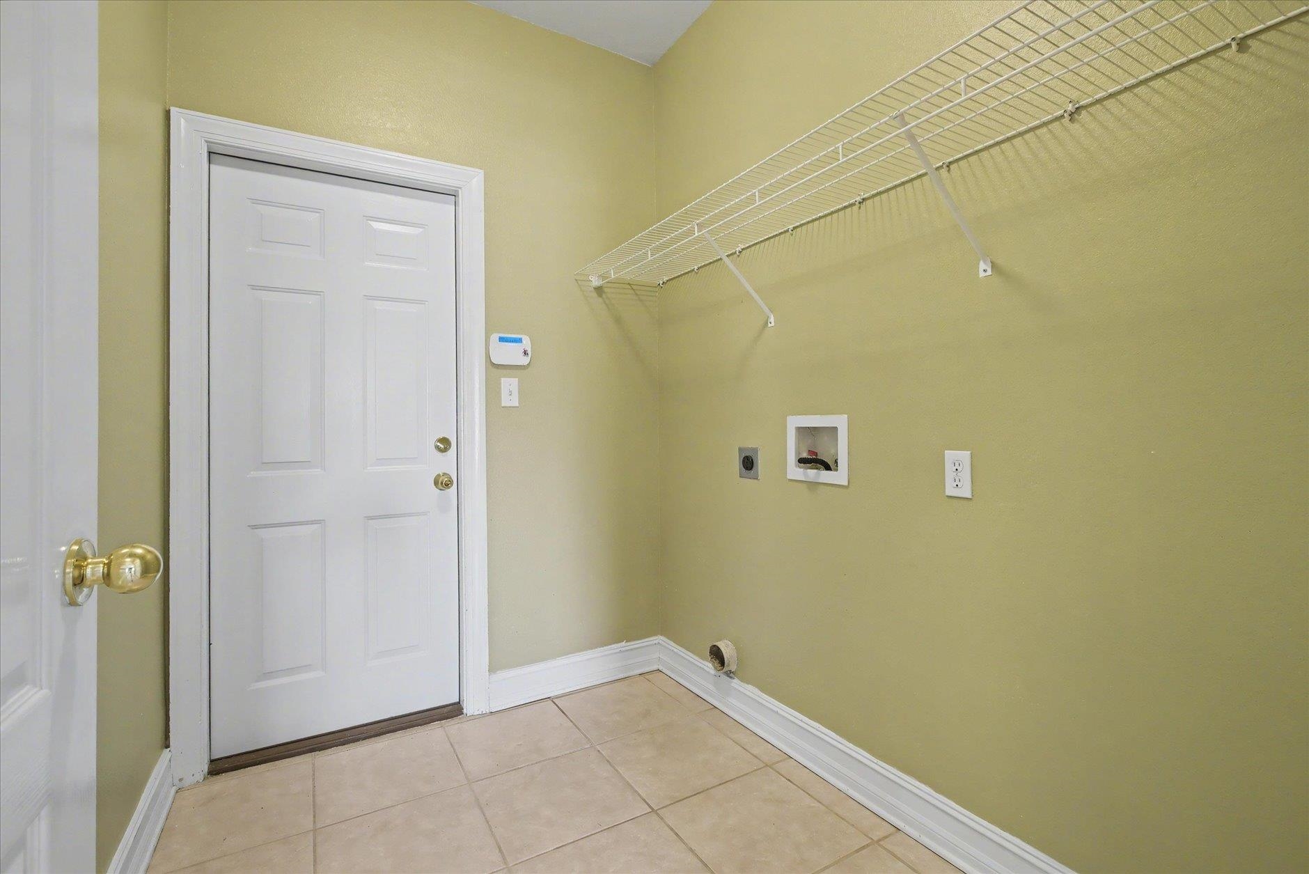 Laundry room with tile flooring, wire shelving, and washer and dryer hookups.