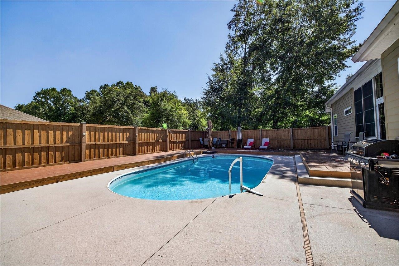 Backyard pool with curved entry steps, wooden privacy fencing, and a concrete patio.