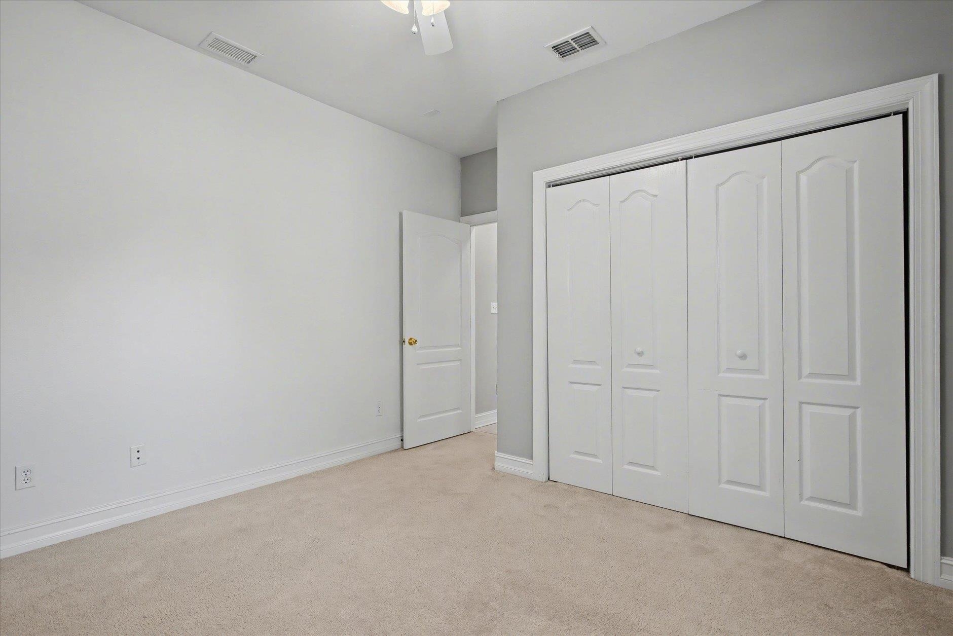 Empty carpeted bedroom with a ceiling fan and large white paneled closet doors.