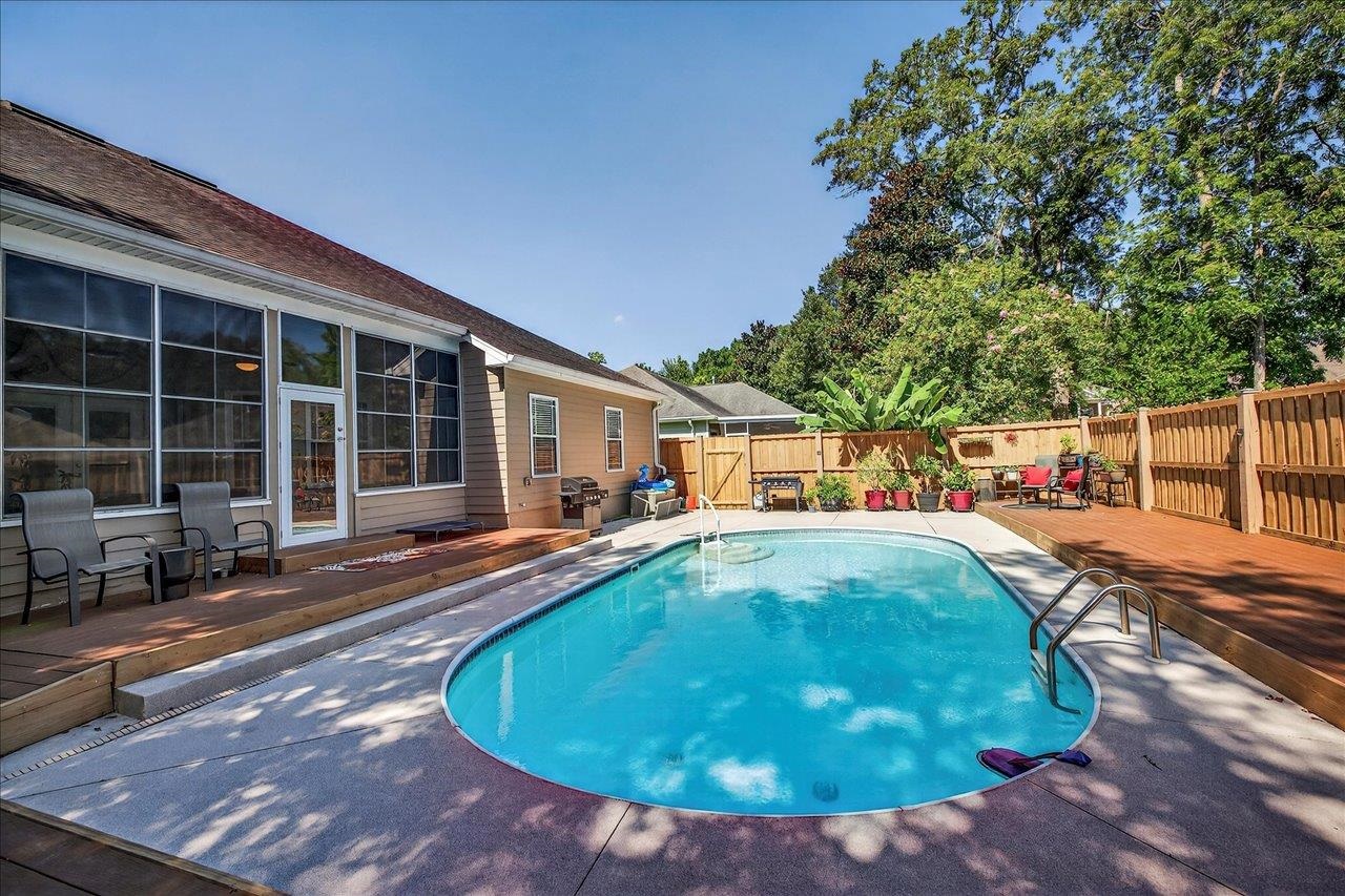 Backyard swimming pool bordered by a wood deck, patio seating, and a privacy fence.